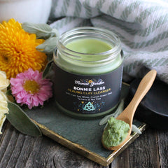 Facial cleanser jar with green contents, wooden spoon, and Mama's Garden label on dark surface