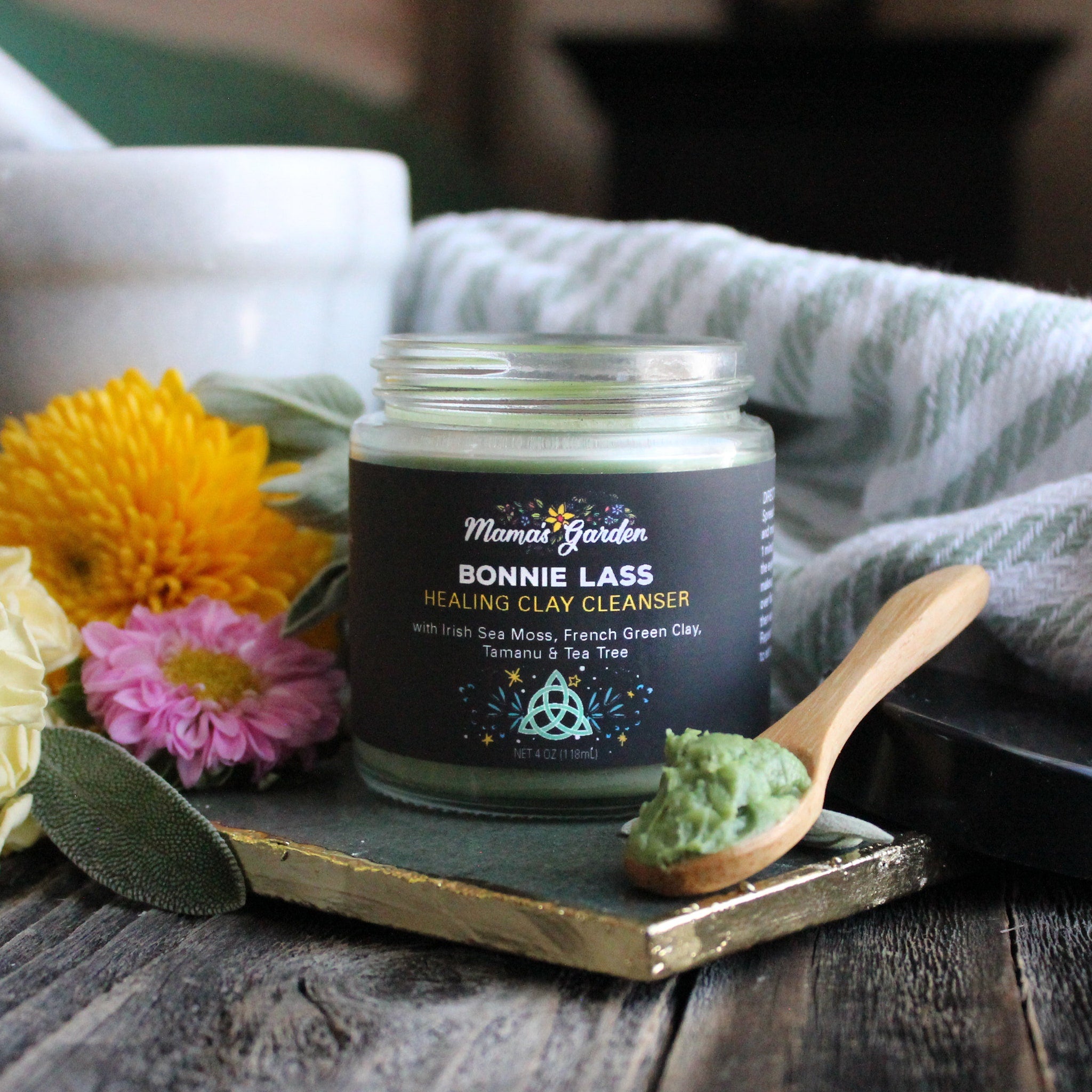 Healing clay cleanser jar with black label, green contents, and wooden spoon on a decorative tray