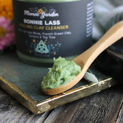 Clay cleanser with green paste on wooden spoon, Mama's Garden label in background, on gold-edged tray