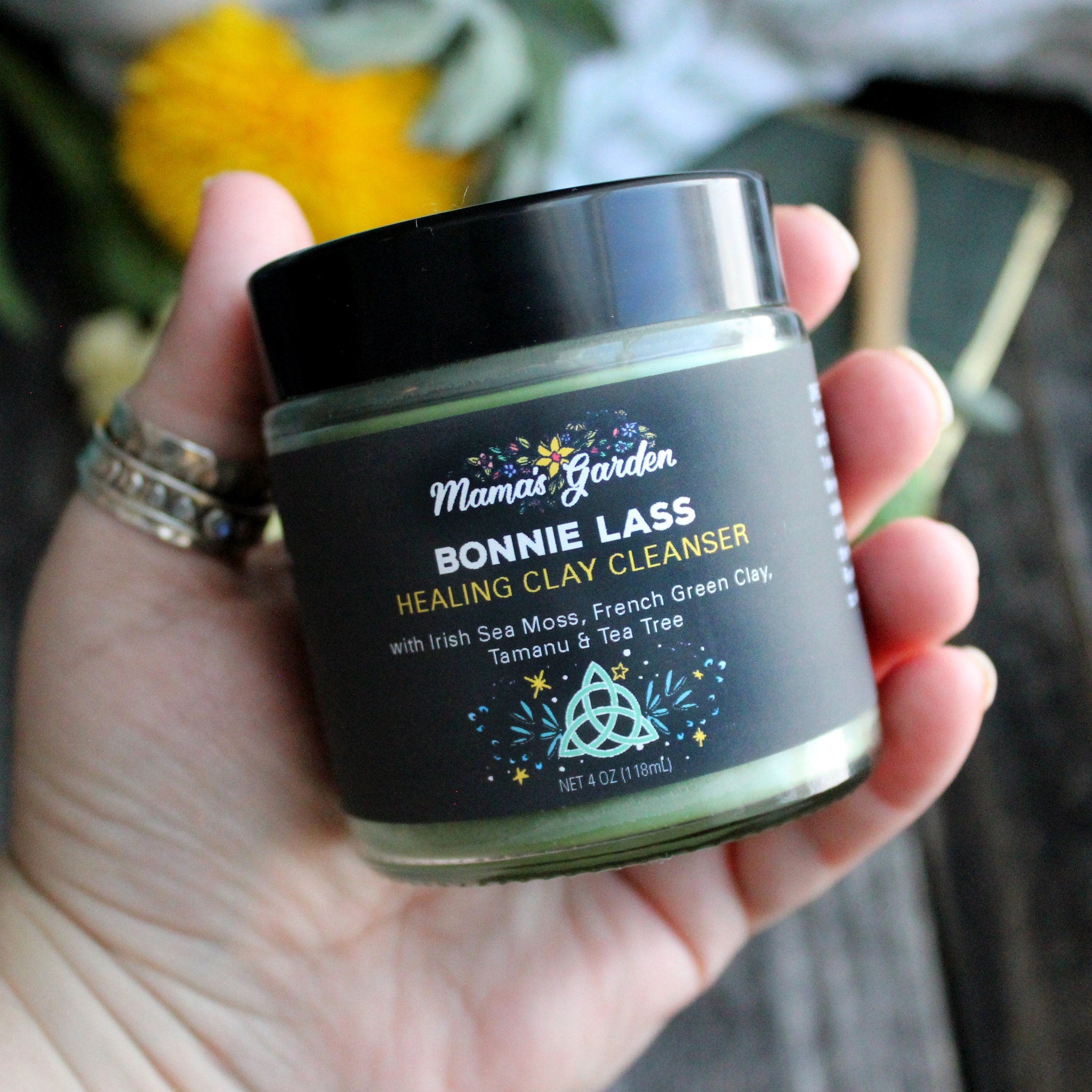 Clay cleanser jar with black label, green contents, and Mama's Garden branding held in hand