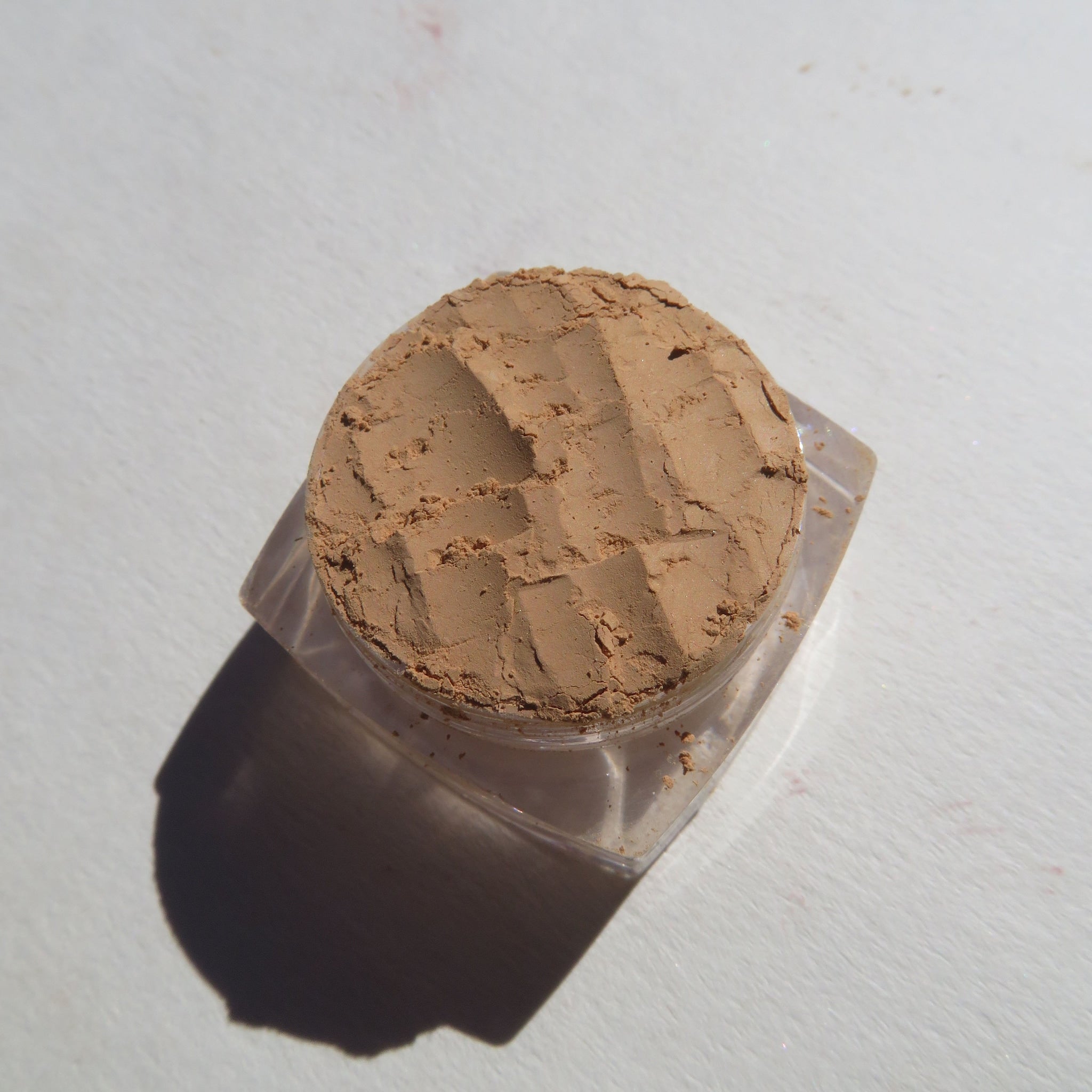 Powdered makeup in tan color with textured surface in clear plastic container