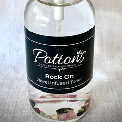Jewel infused toner bottle, clear glass, black label with HerbalistPotions text, and colorful stones inside