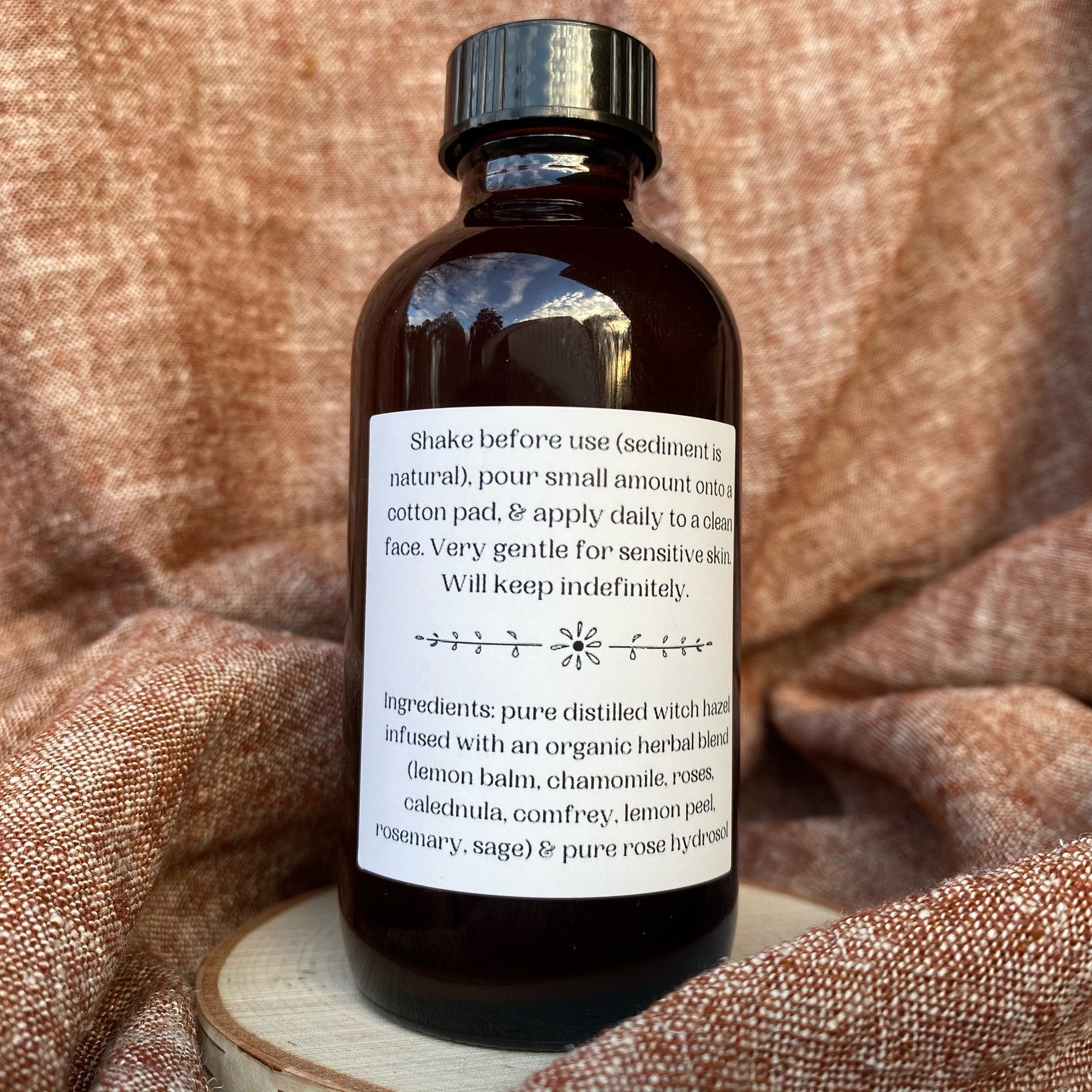 Facial toner bottle, dark brown glass with black cap, white label with text on wood base