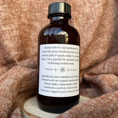 Facial toner bottle, dark brown glass with black cap, white label with text on wood base