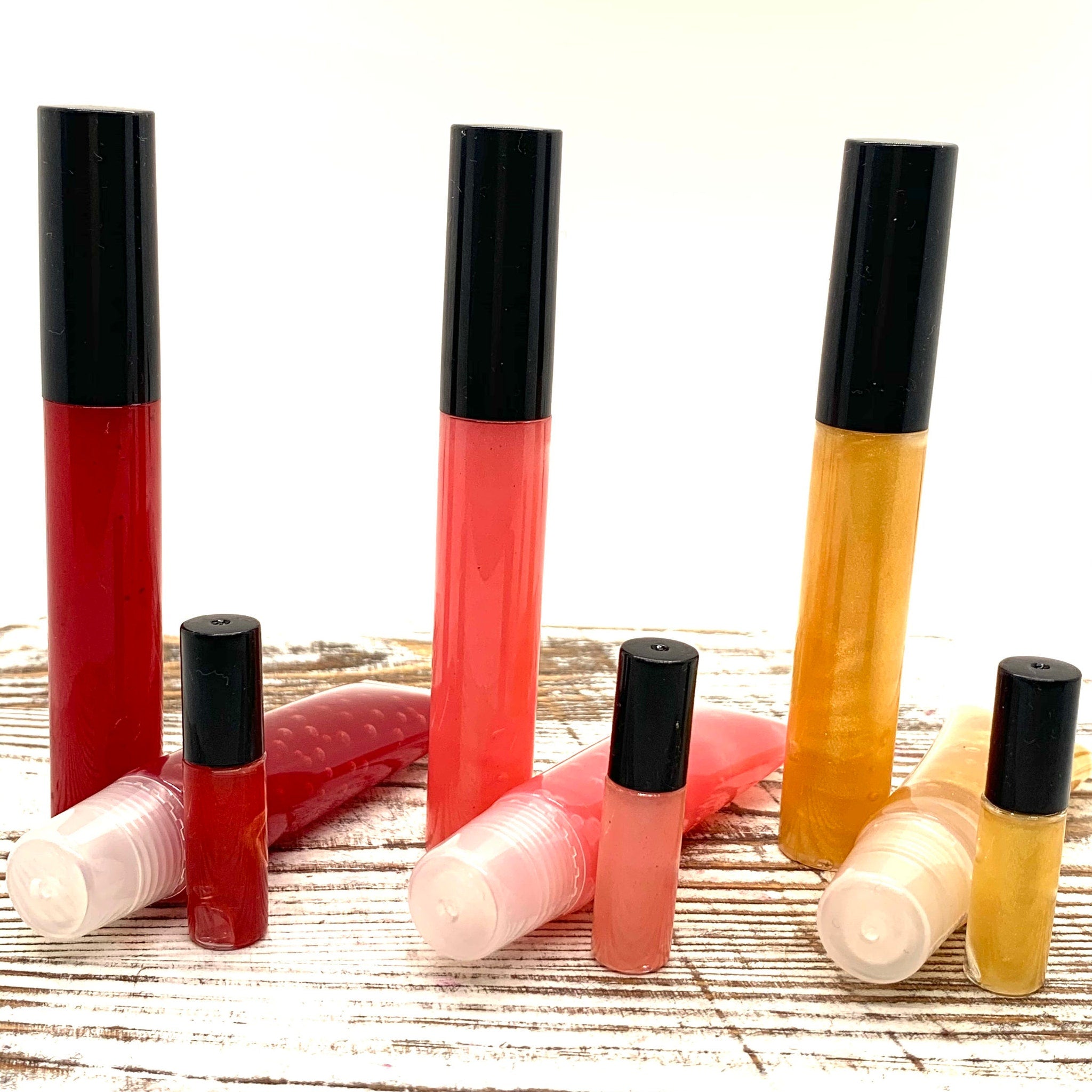 Lip gloss tubes with black caps and various colors, including red, coral, and gold