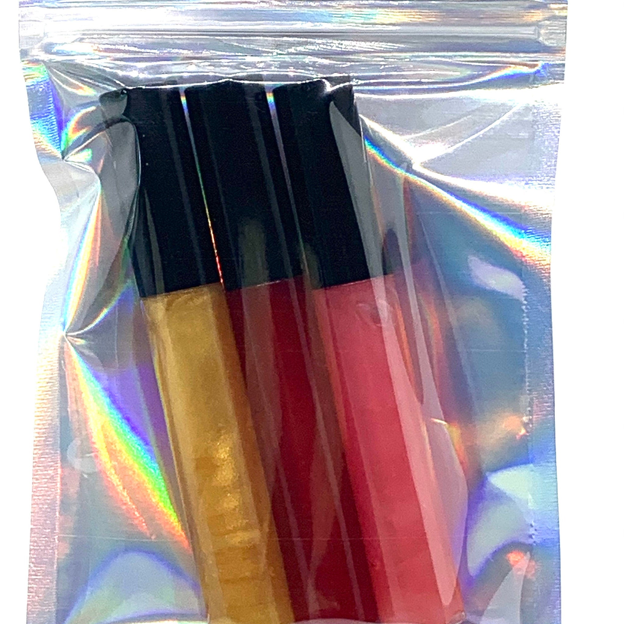 Lip gloss tubes in clear plastic bag, gold, red, and pink colors with black caps