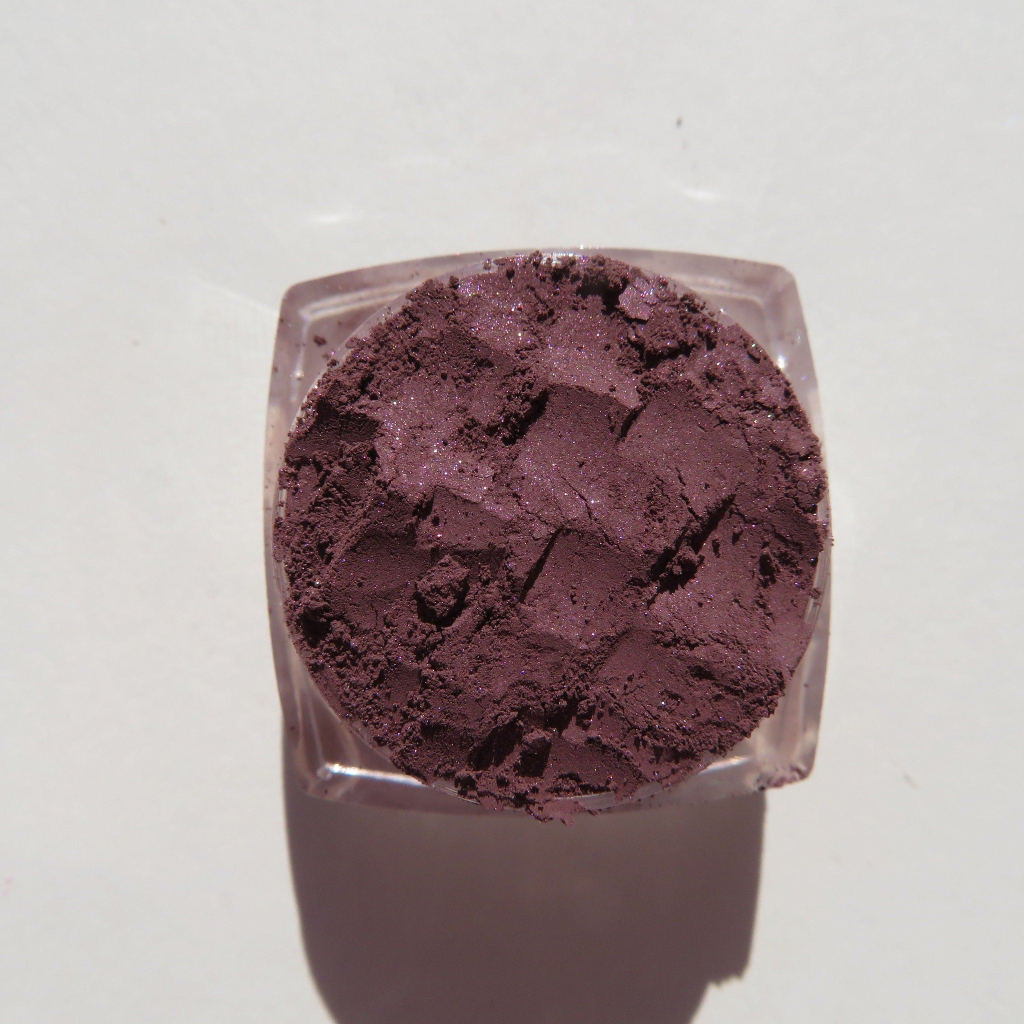 Eyeshadow powder in dark purple with glitter, in a clear plastic container