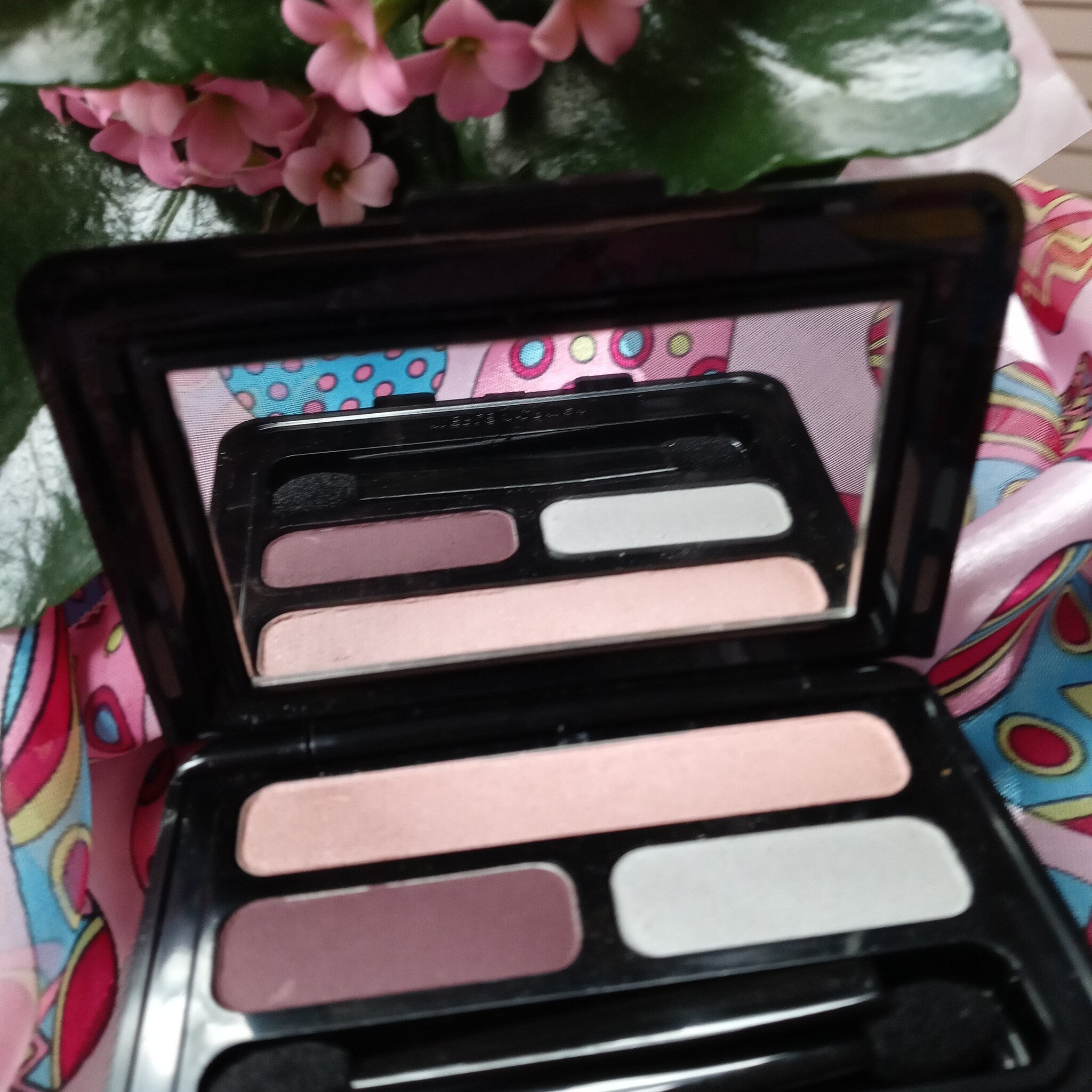 Eyeshadow palette with black plastic case, pink, white, and purple shades visible
