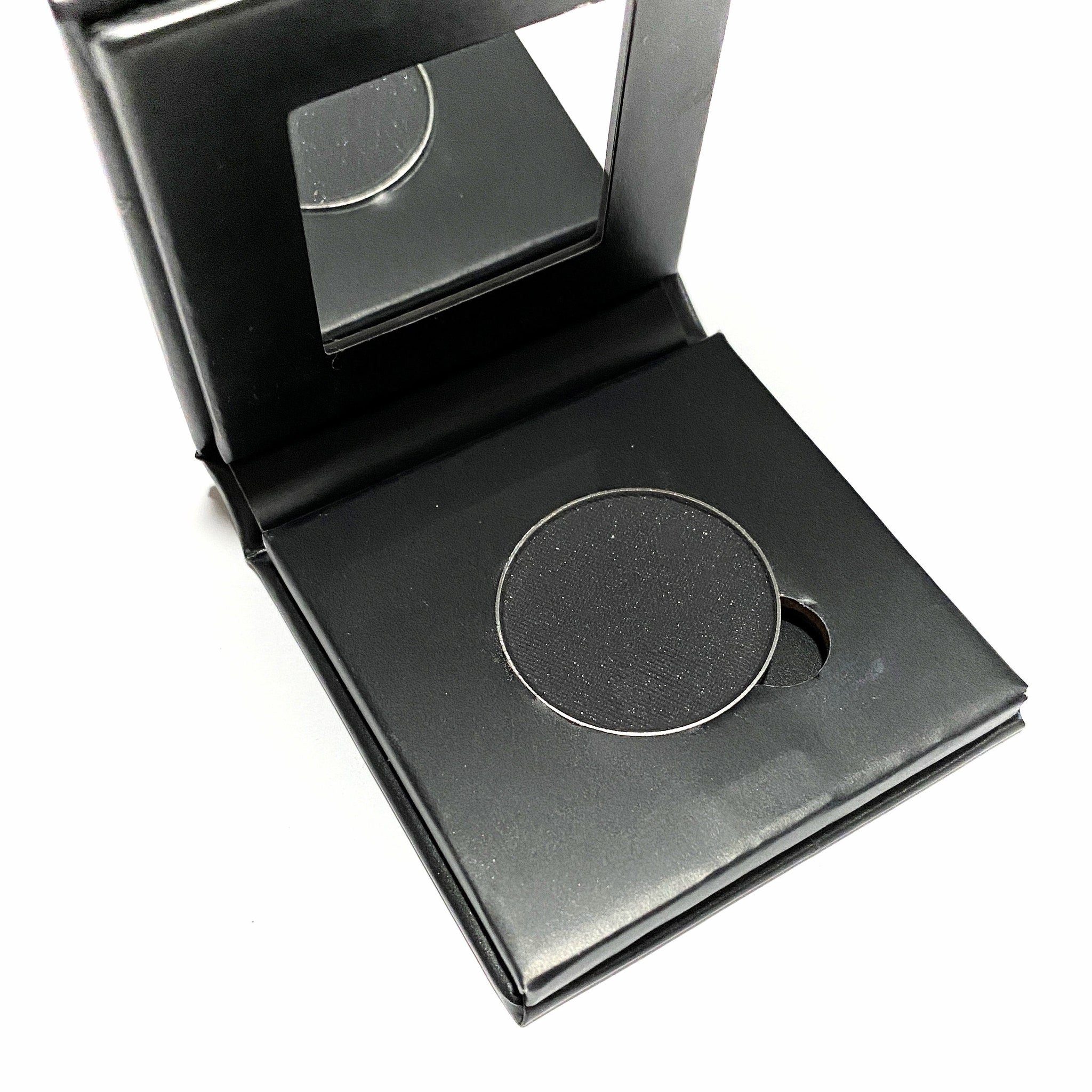 Side view of jet black mineral eye shadow compact showing matte paperboard texture and hinge detail