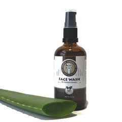 Face wash bottle with brown glass, black pump, and green aloe leaf beside it
