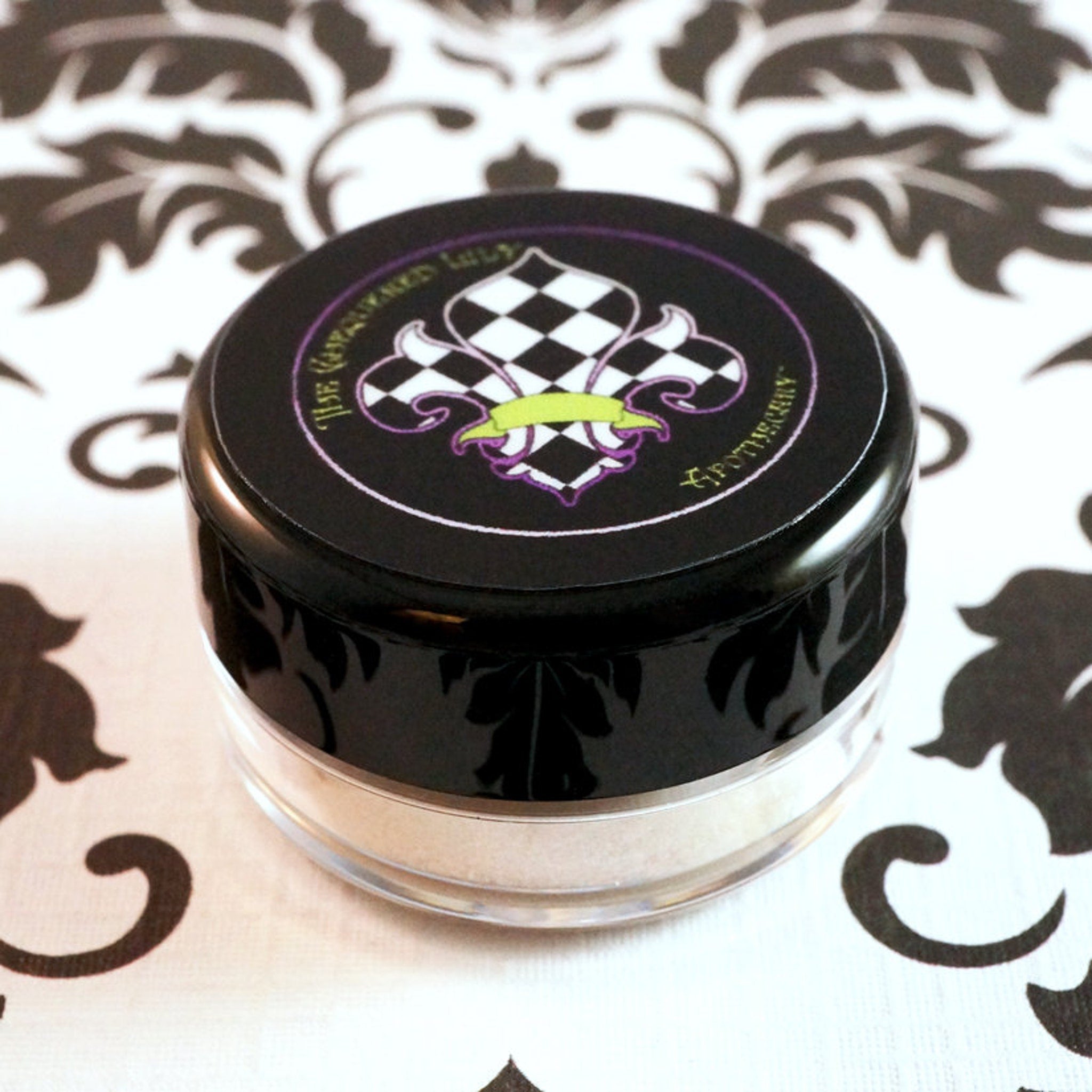 Side view of loose vanilla ivory eyeshadow with silver-white shimmer in a clear jar, showcasing glitter texture.