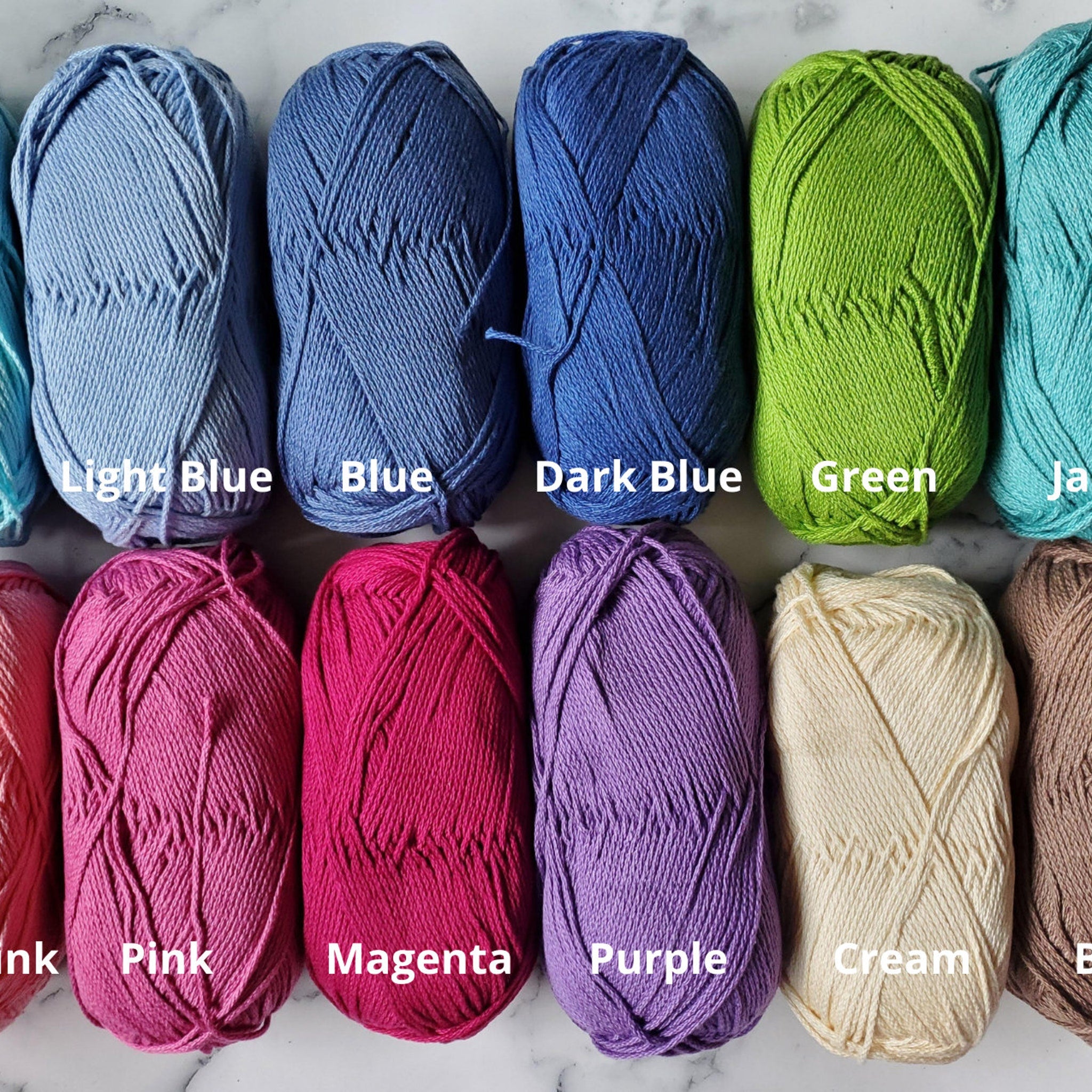 Yarn skeins in various colors, including blue, green, pink, and cream, arranged on a marble surface