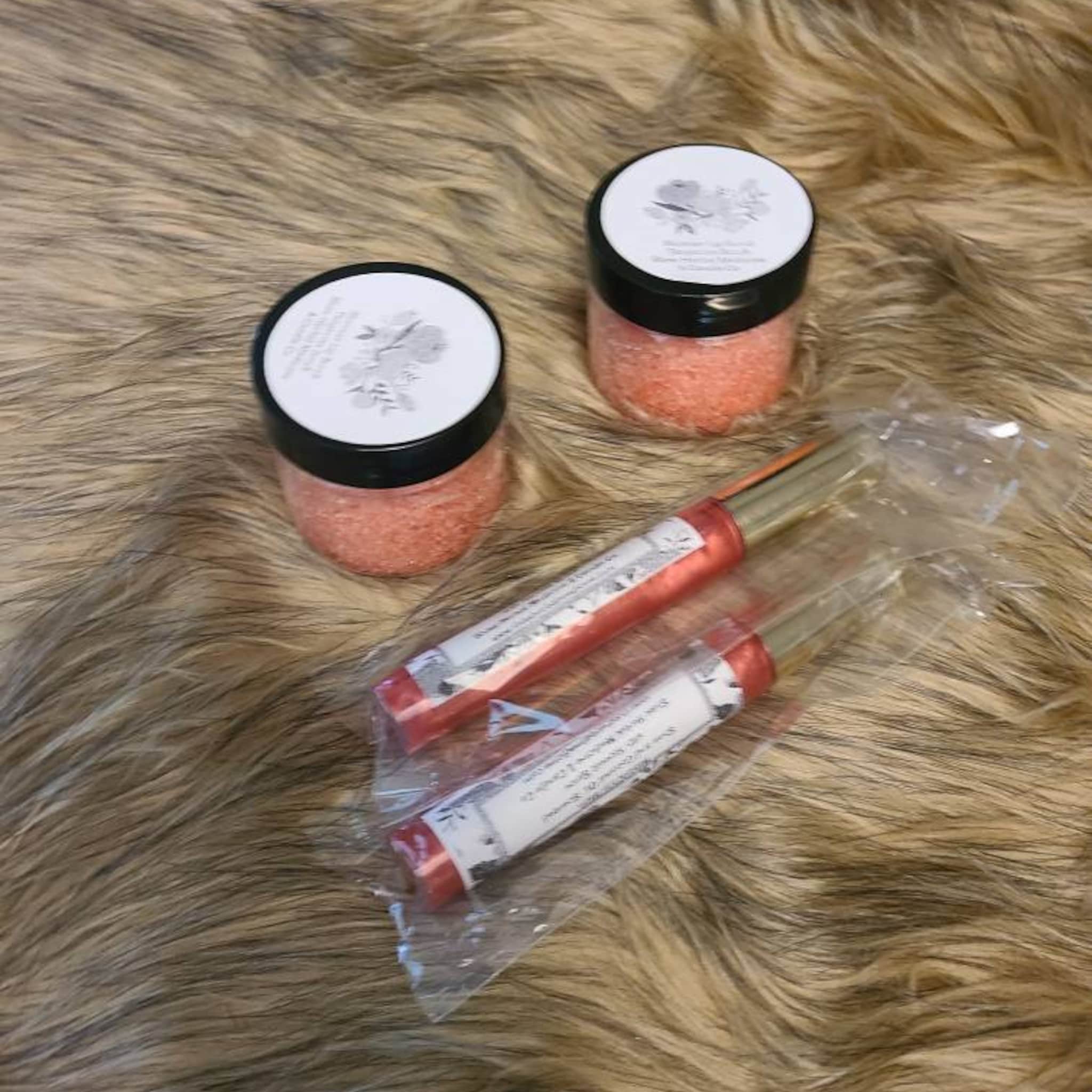 Lip gloss and jars with pink contents, black lids, and white labels on faux fur background
