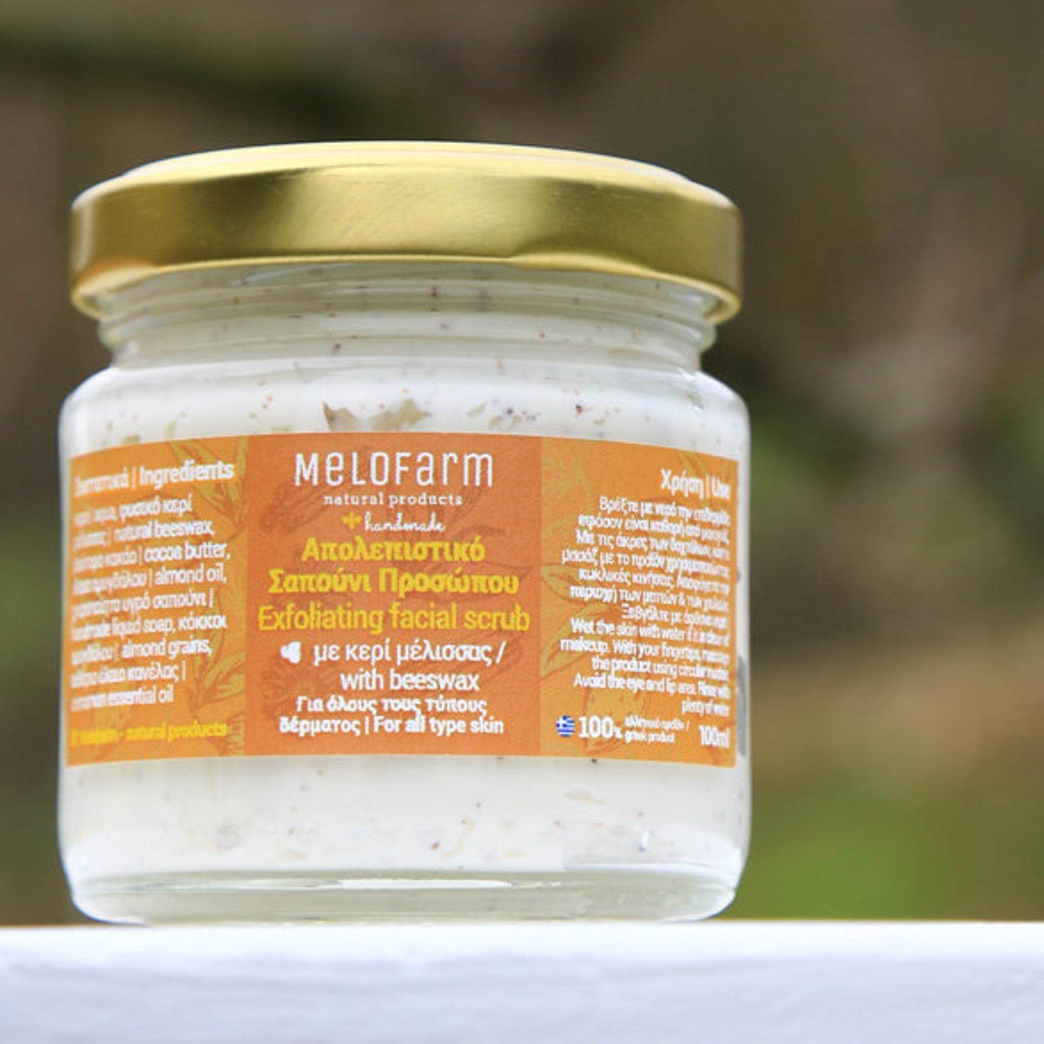 Facial scrub in glass jar with gold lid, white cream, and orange label with MELOFARM text.