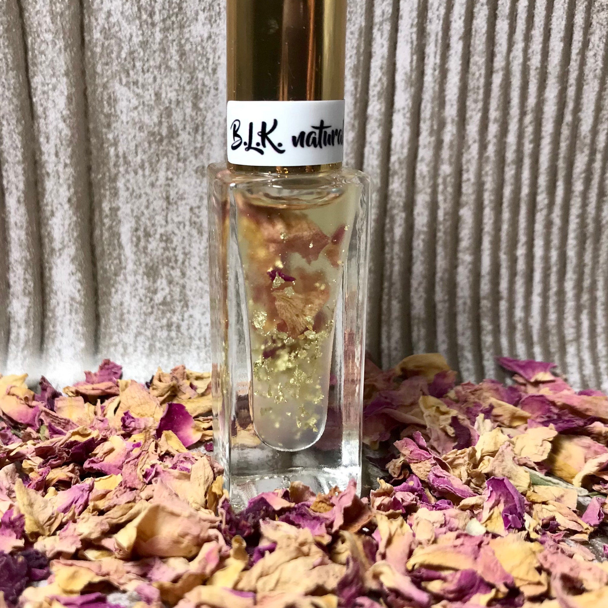 B.L.K. natural perfume bottle with gold cap, clear glass, and gold flakes, surrounded by dried petals