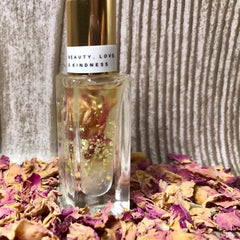 Perfume bottle with gold cap and label, clear glass, gold flakes, and dried rose petals