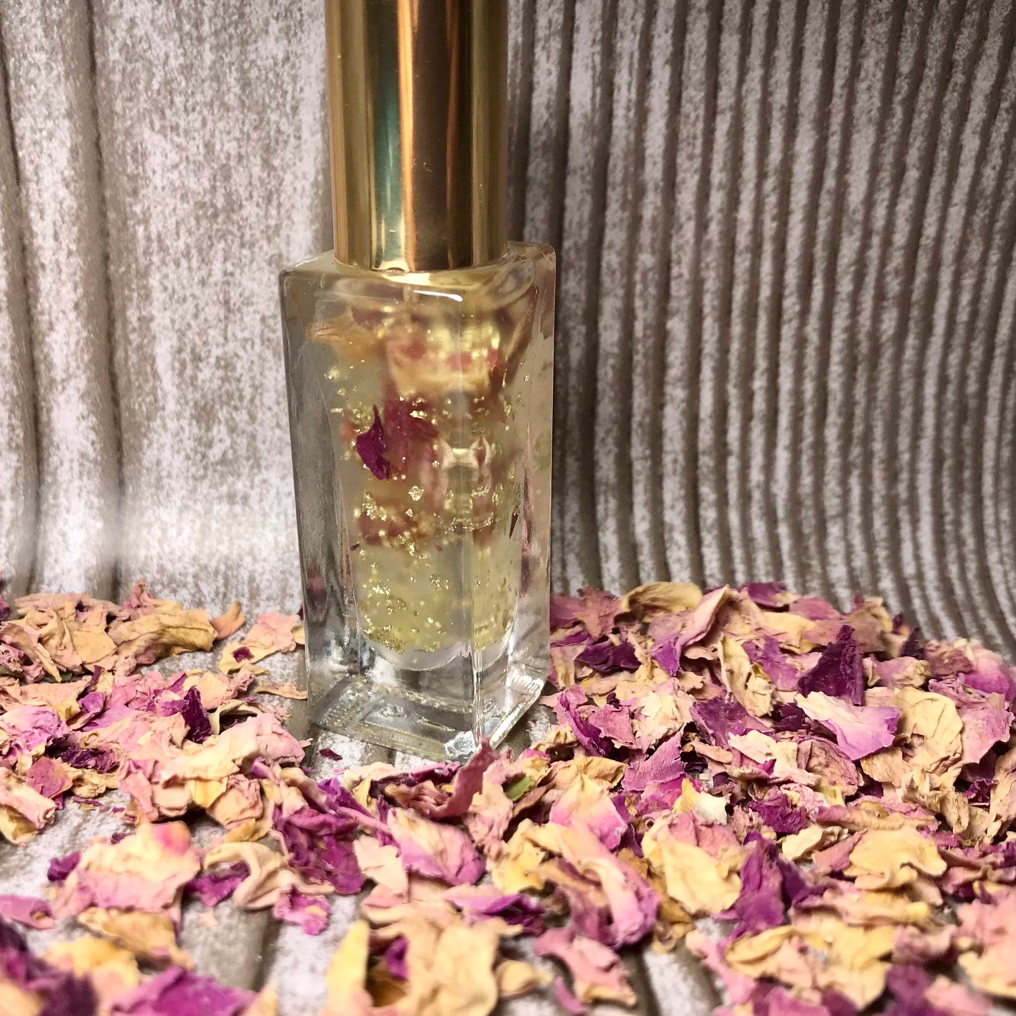 Perfume bottle with gold cap, clear glass, and rose petals around it