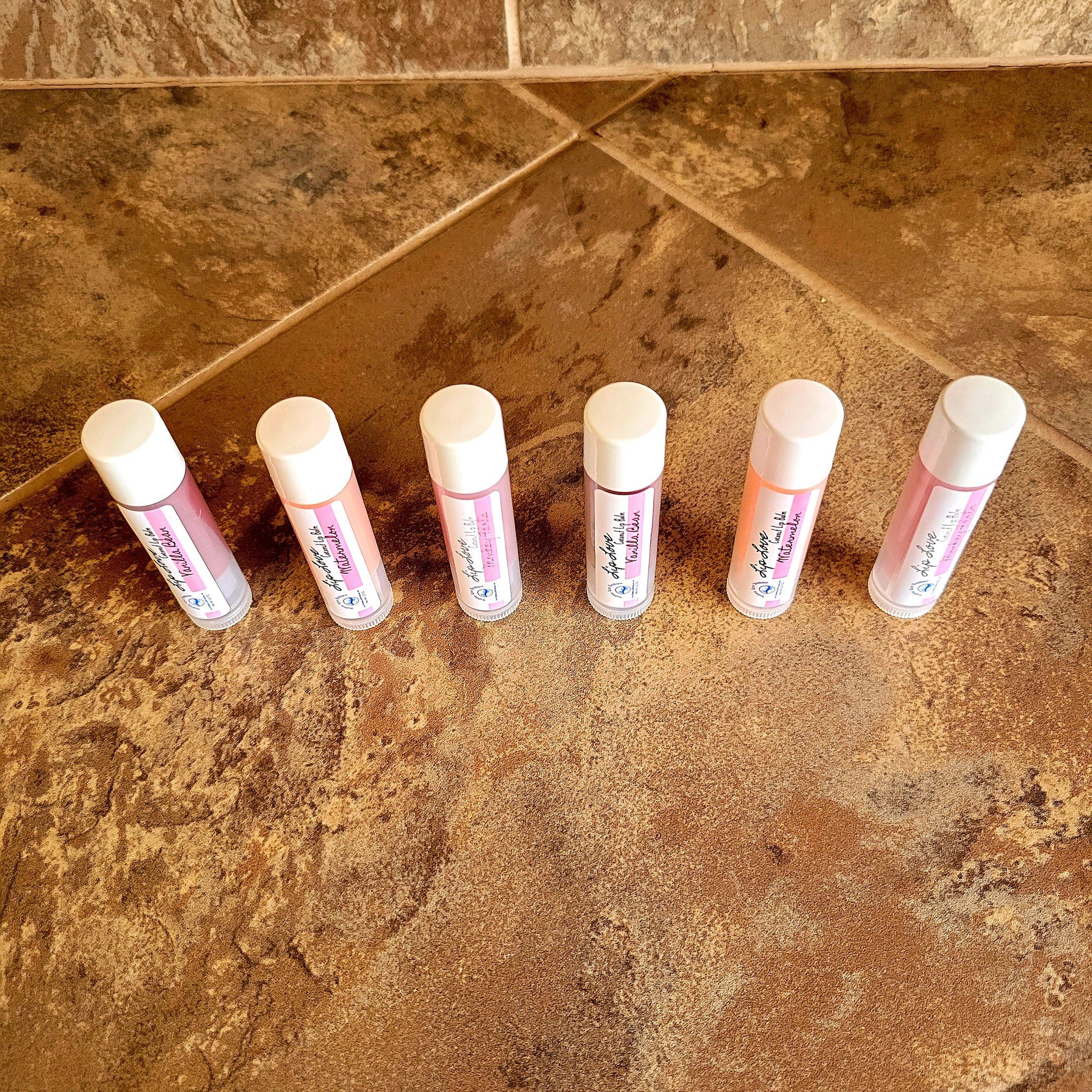 Lip balm tubes with white caps, pink and white labels, arranged on brown tile surface