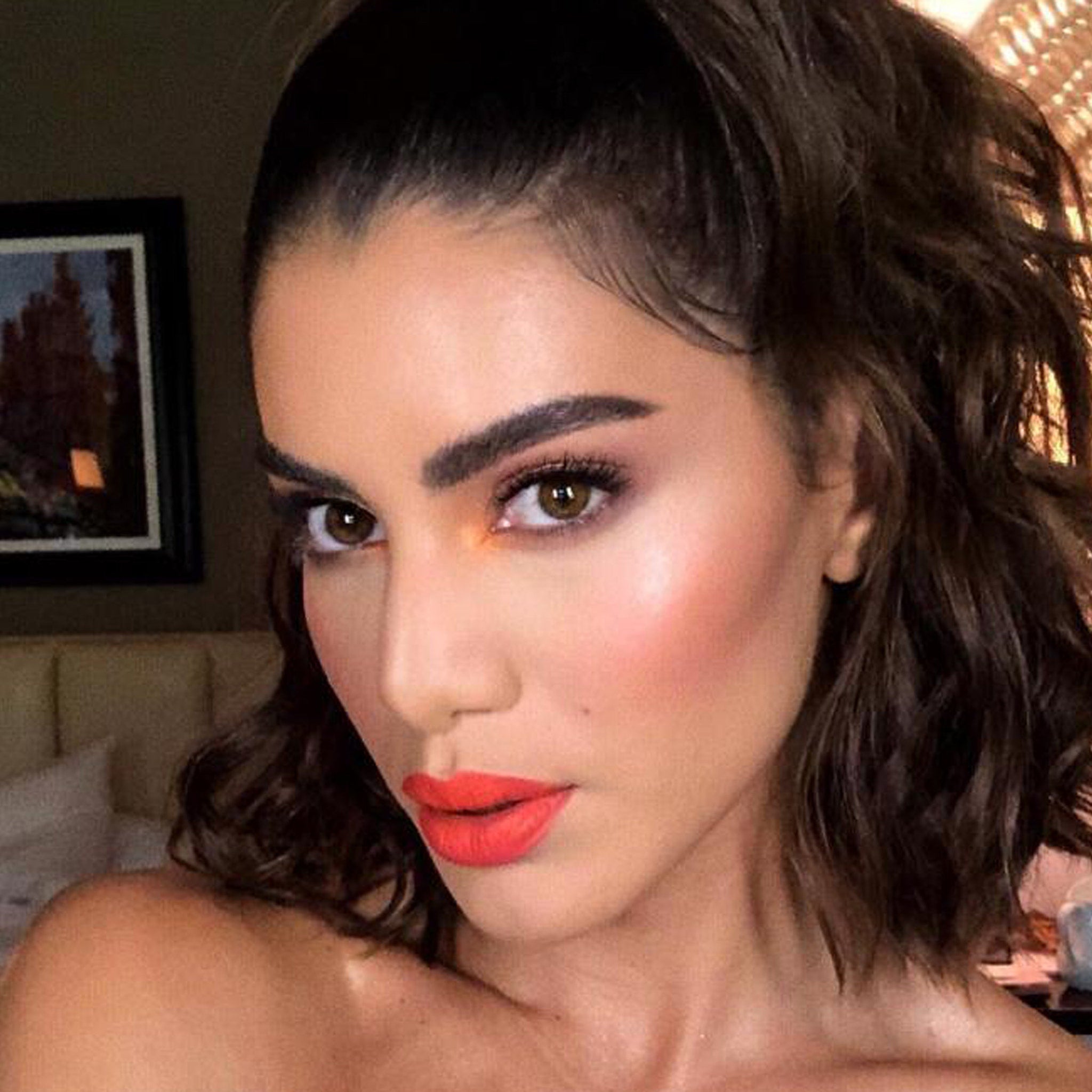 Makeup look with orange eyeshadow, red lipstick, and dark brown hair in a half-up style