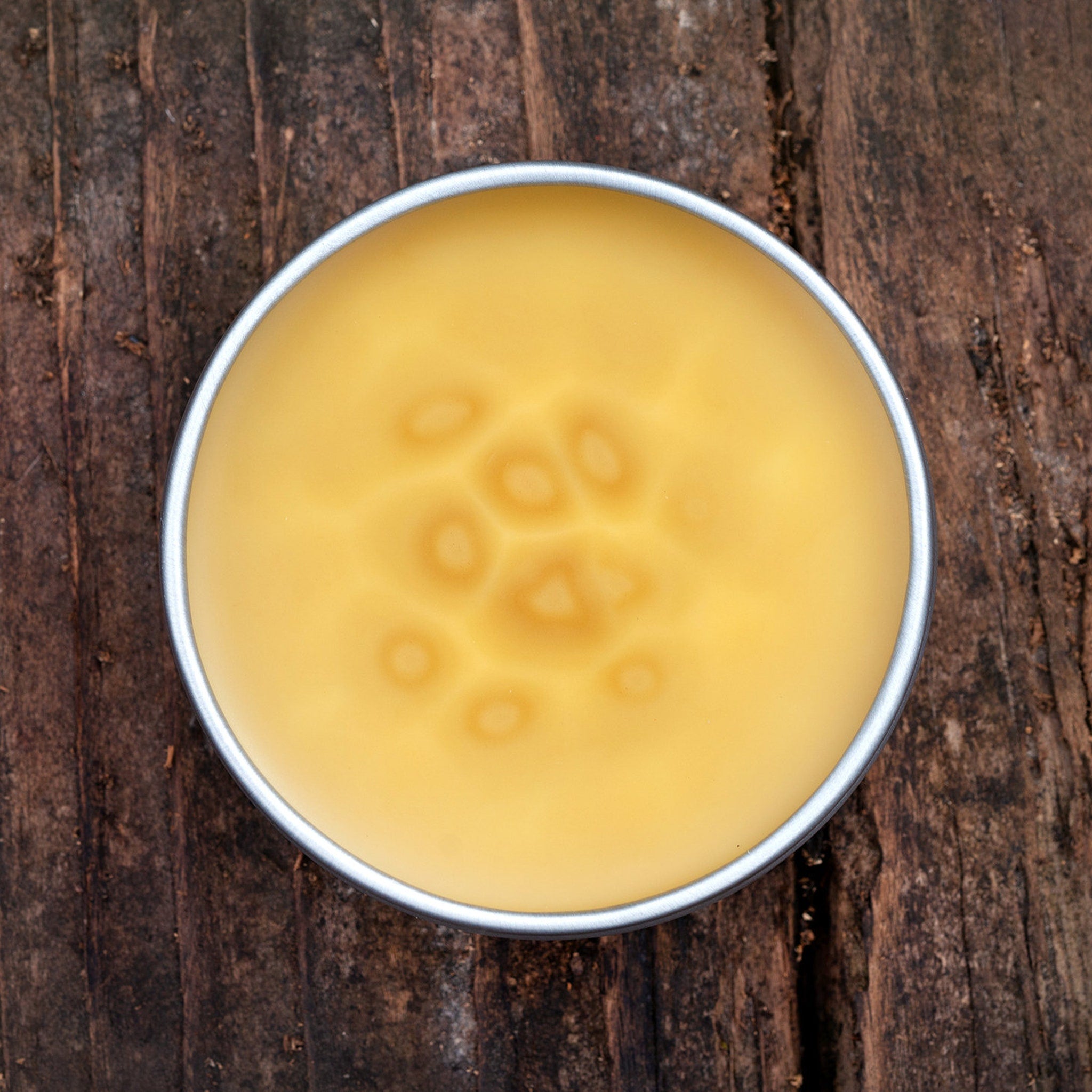 Yellow balm in silver tin on wood surface with pattern detail