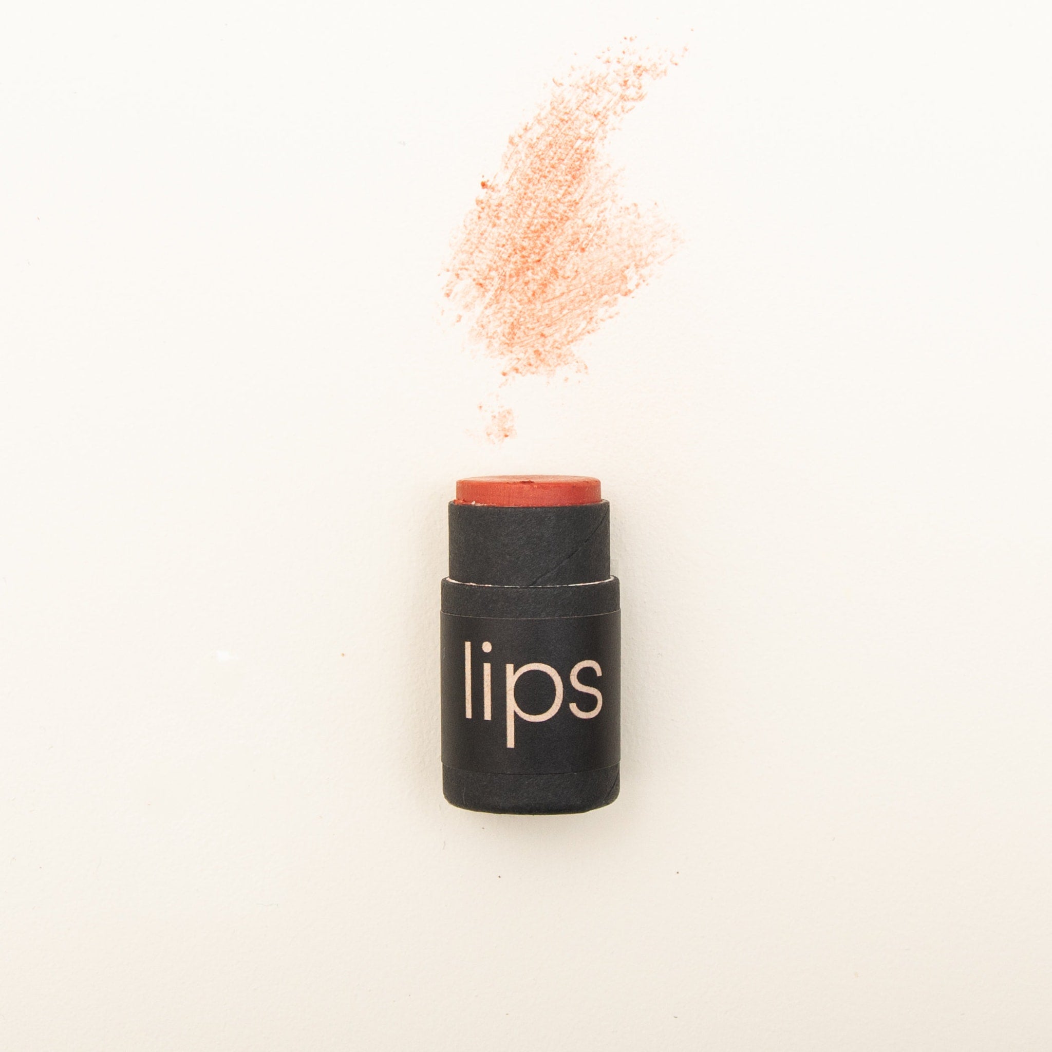 Lipstick with orange color, black paper tube, "lips" text on tube, and lipstick swatch