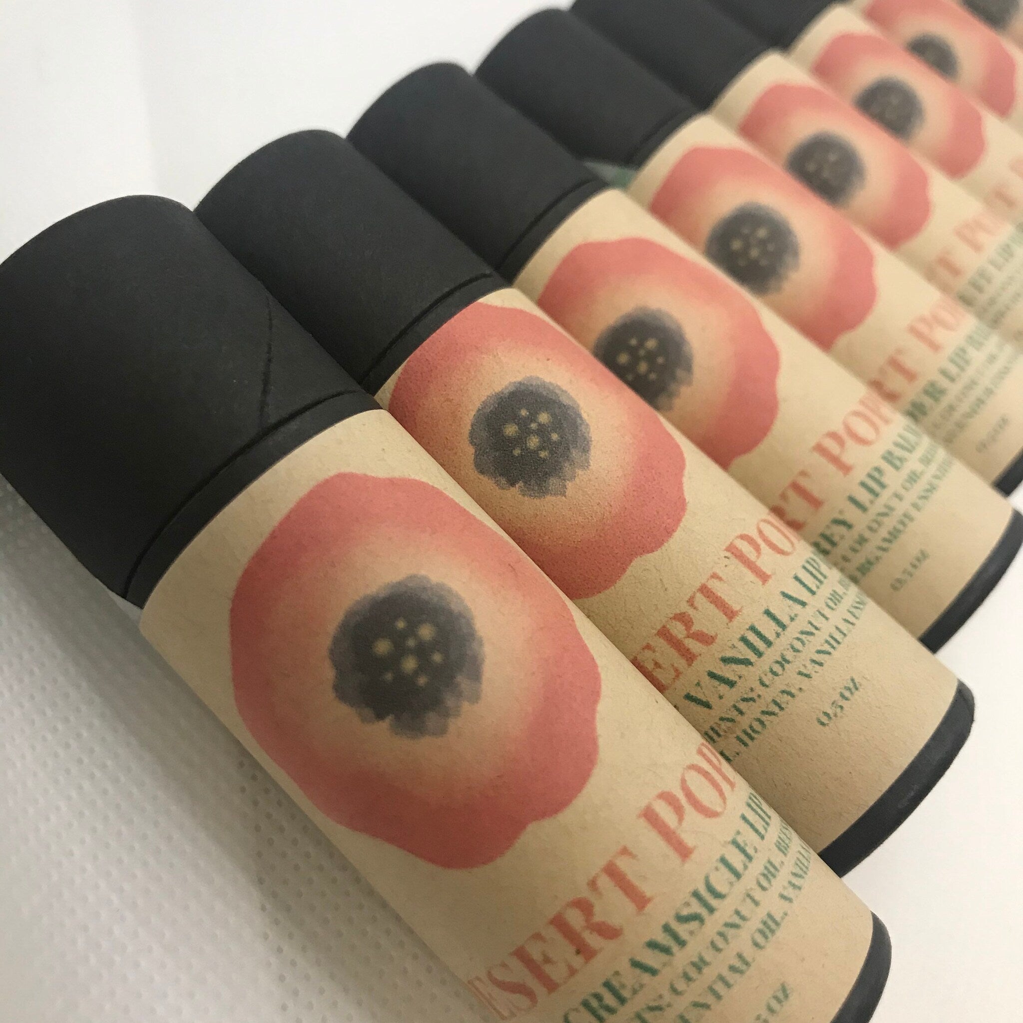 Lip balm tubes with black caps, beige paper, and red floral design, Desert Port brand