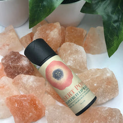 Lip balm tube with black cap, floral label, and pink flower, on pink rock salt