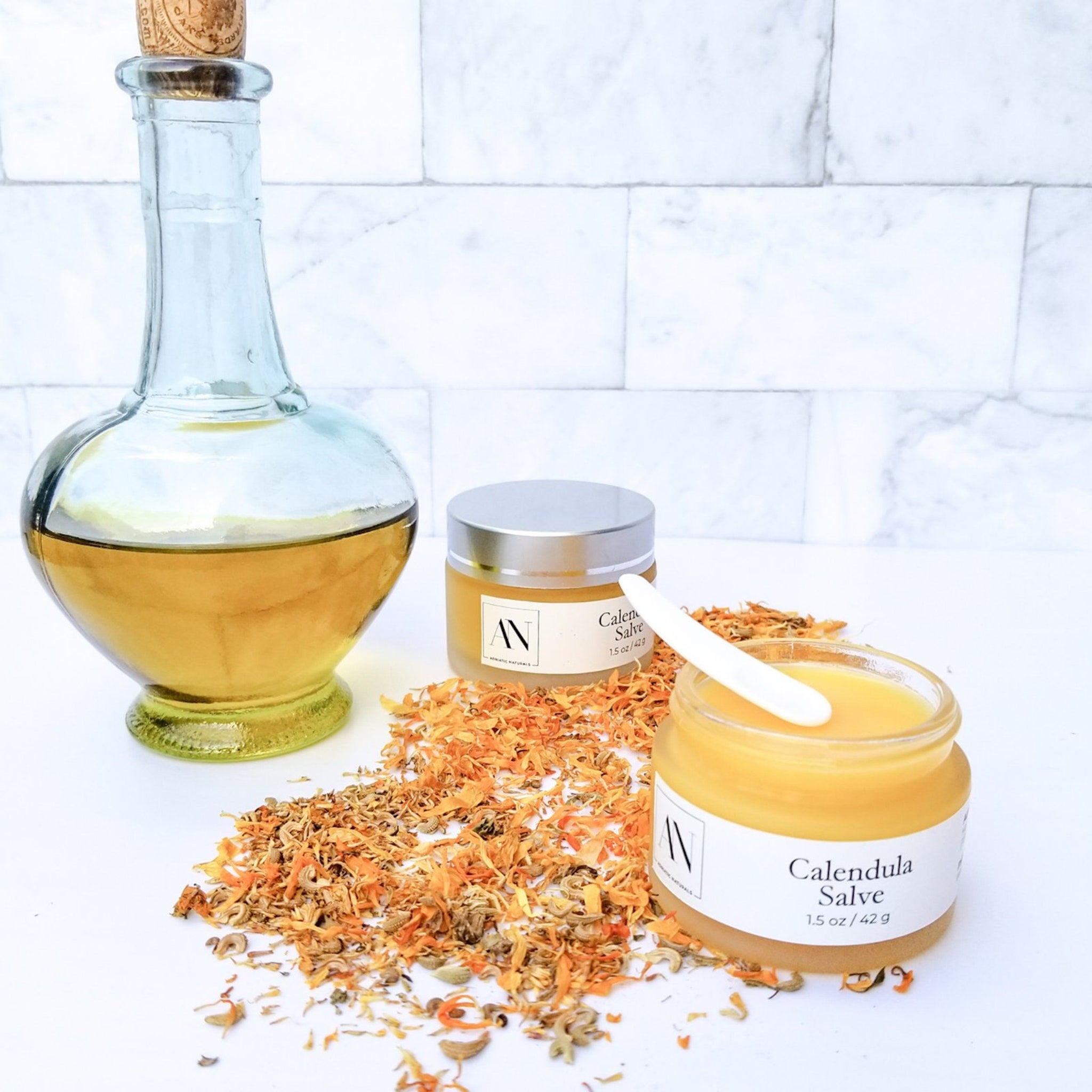 Calendula salve in glass jar with white label, yellow contents, and white spoon on white surface