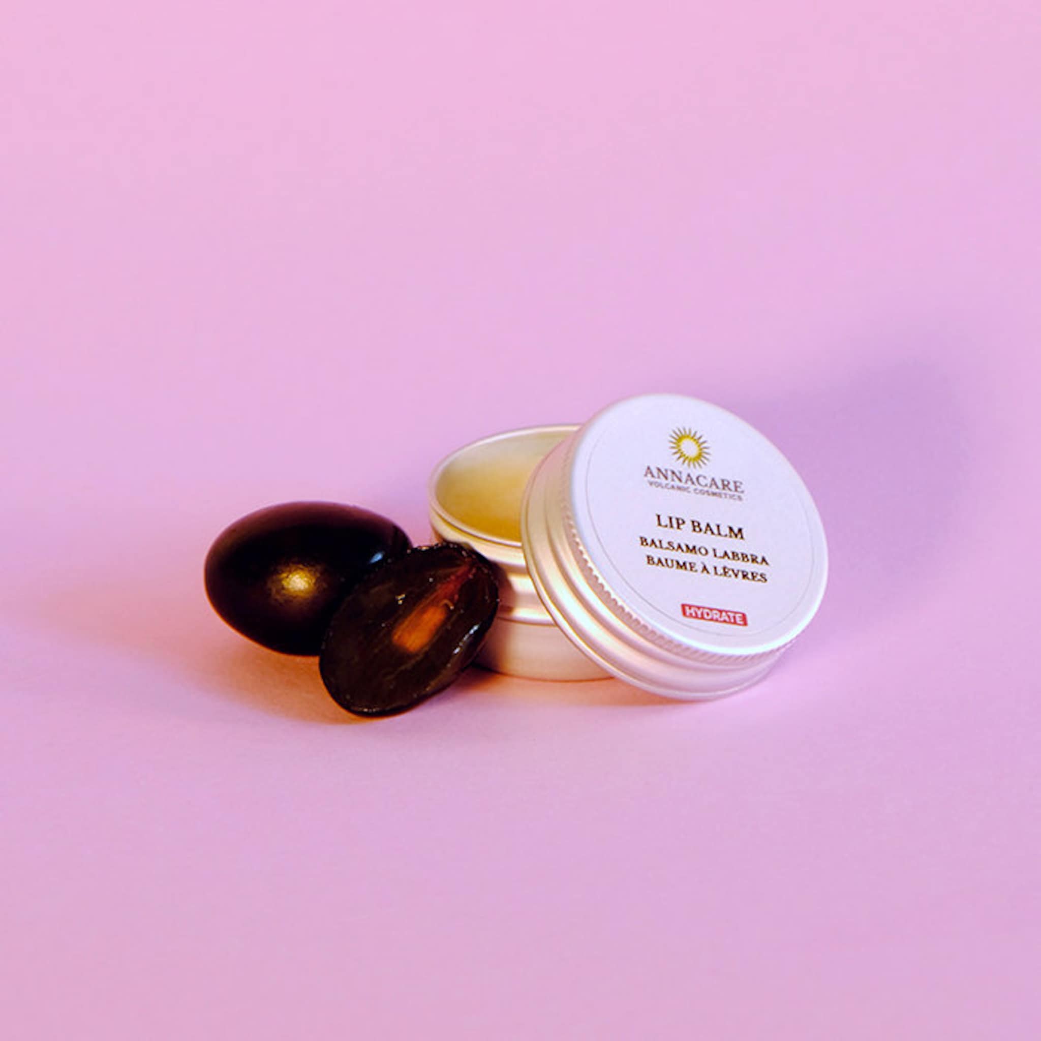 Lip balm in silver tin with Annacare label, dark fruit and pink background