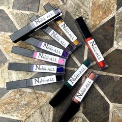 Lipstick tubes in various colors with black caps and Natur-ALL label, arranged on stone surface