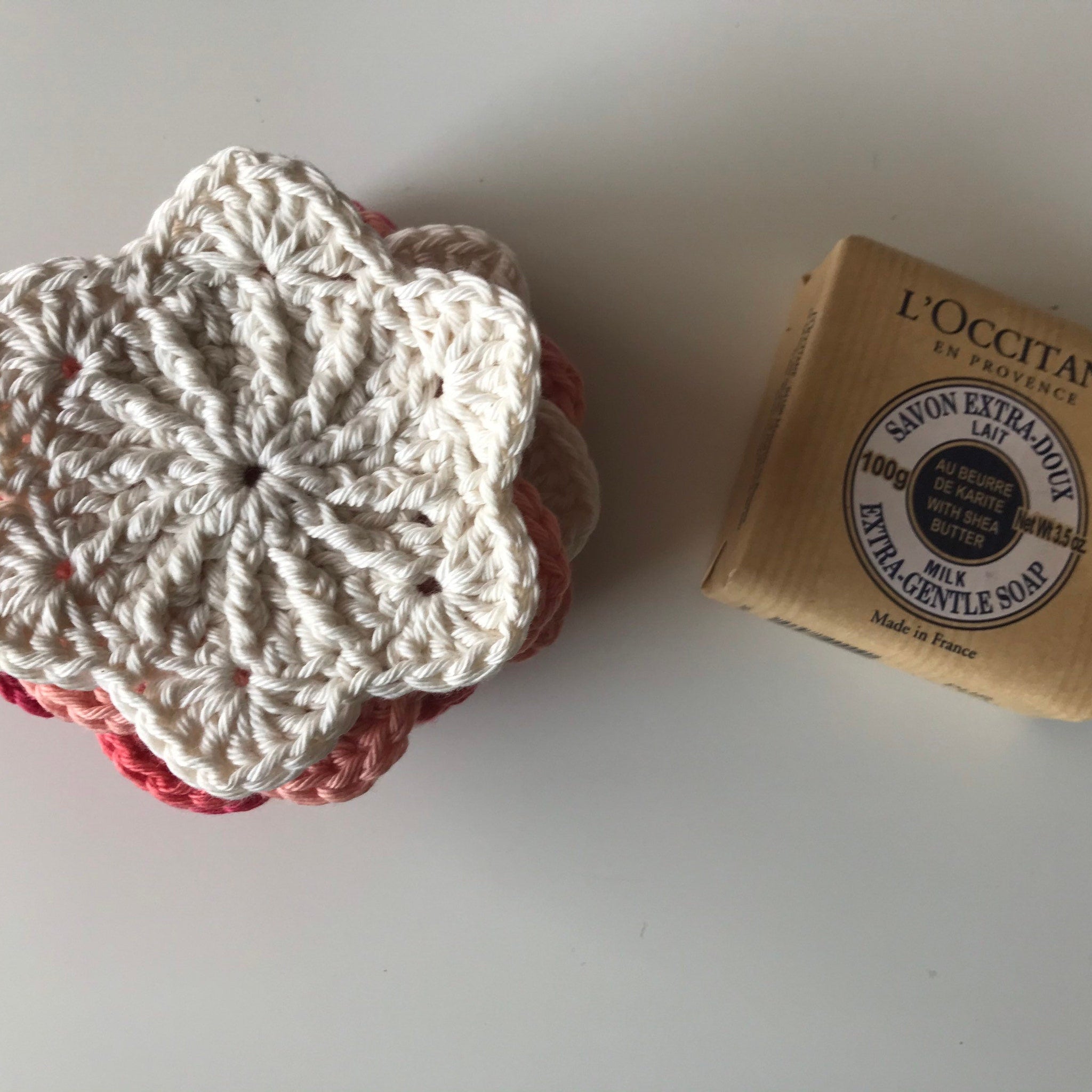 Crochet coasters with white, pink, and peach yarn, next to L'Occitane soap bar