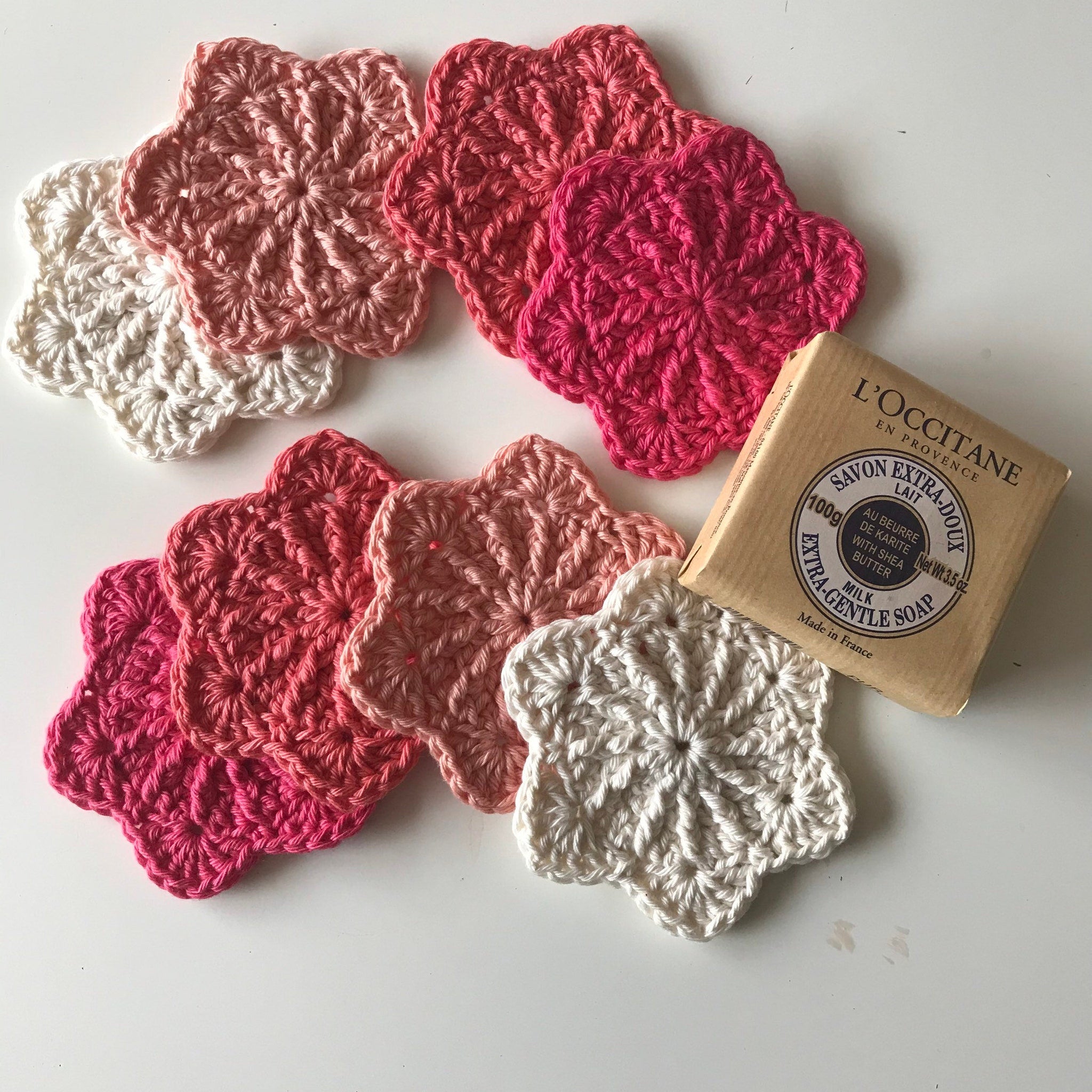 Crochet coasters in white, pink, and coral colors with L'Occitane soap next to them