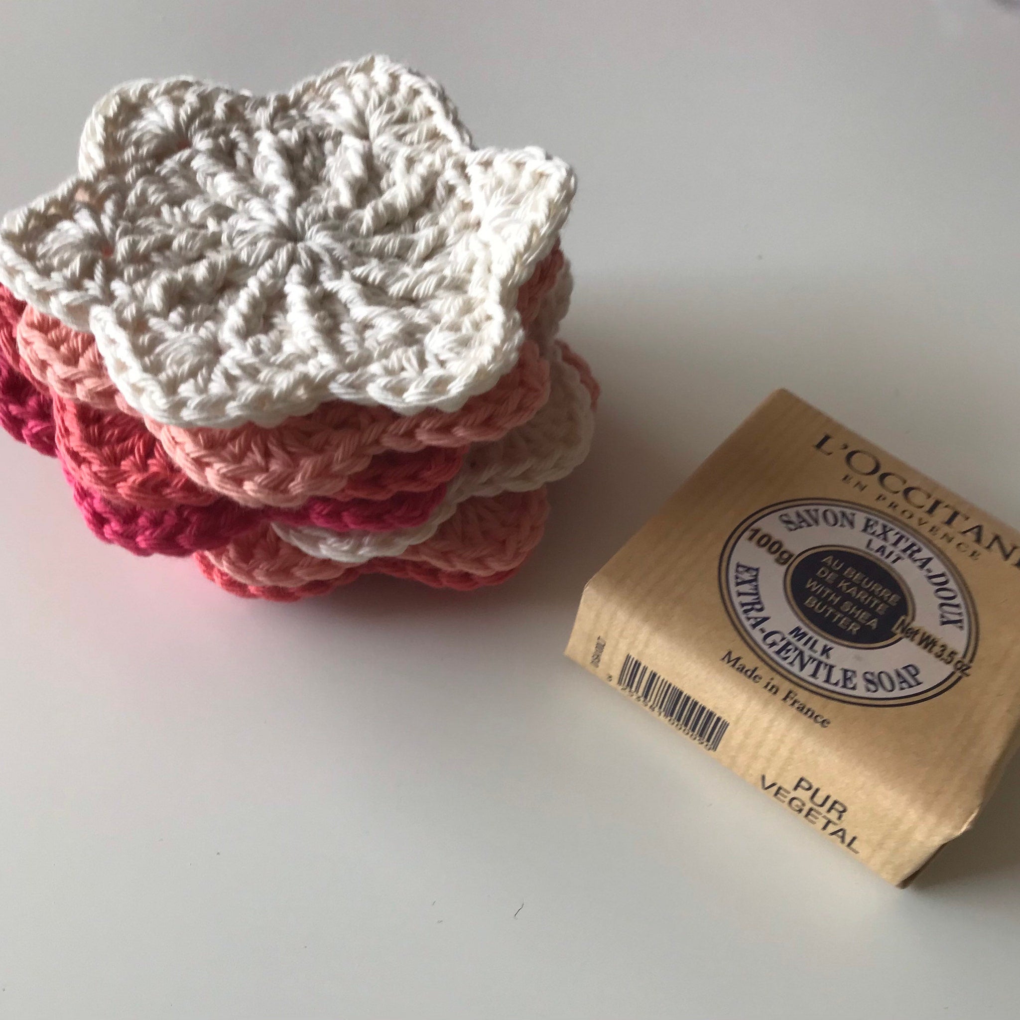 Crochet coasters in white, pink, and red stacked with L'Occitane soap on a white surface