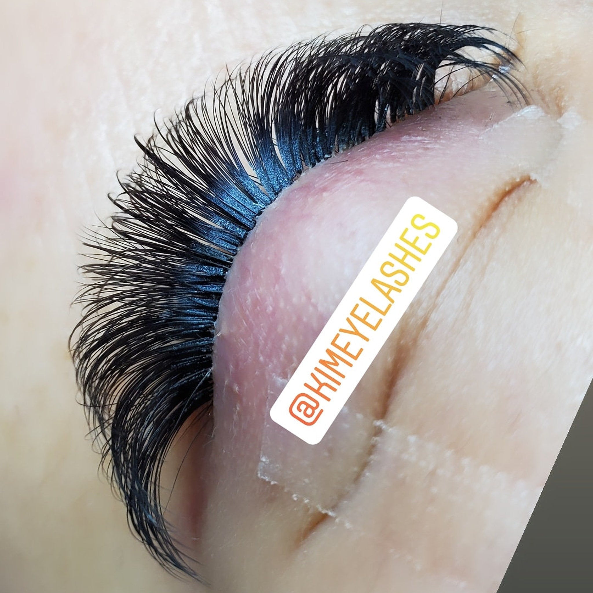 Eyelash extensions with black, curved lashes and @KIMEYELASHES branding on eyelid