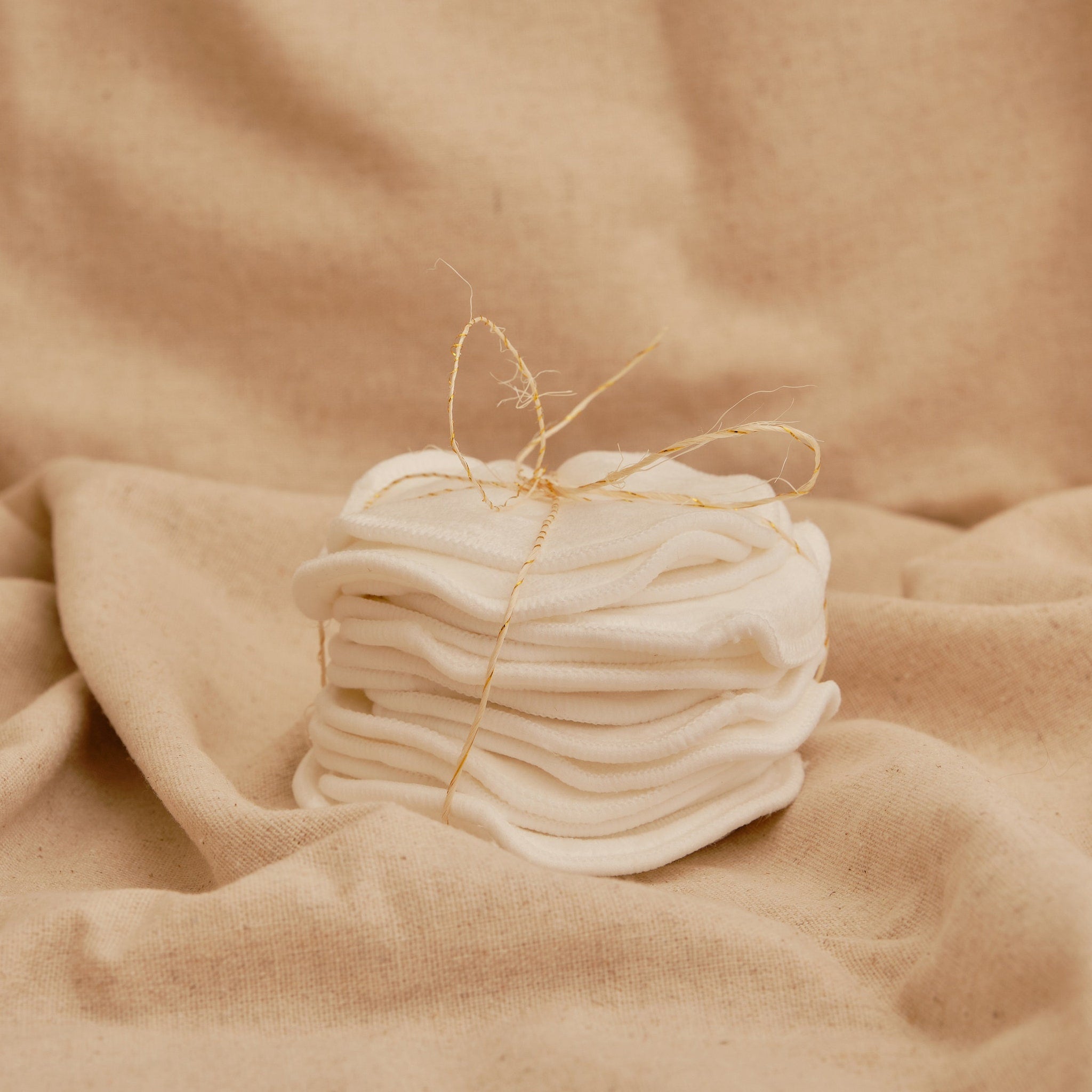 Makeup remover pads, white cotton rounds tied with twine, stacked on beige fabric