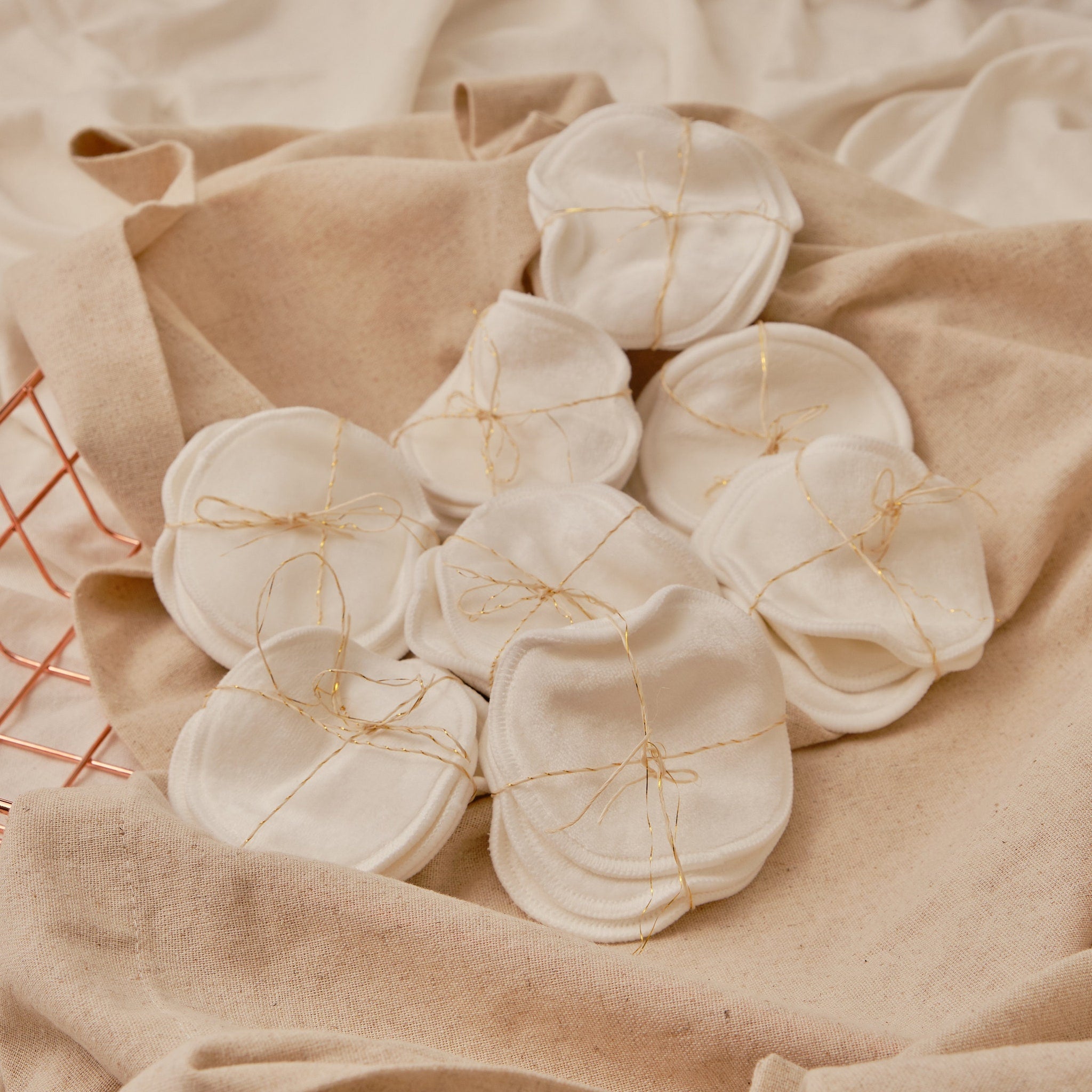 Reusable cotton pads, white circular pads, tied with gold string, on beige fabric