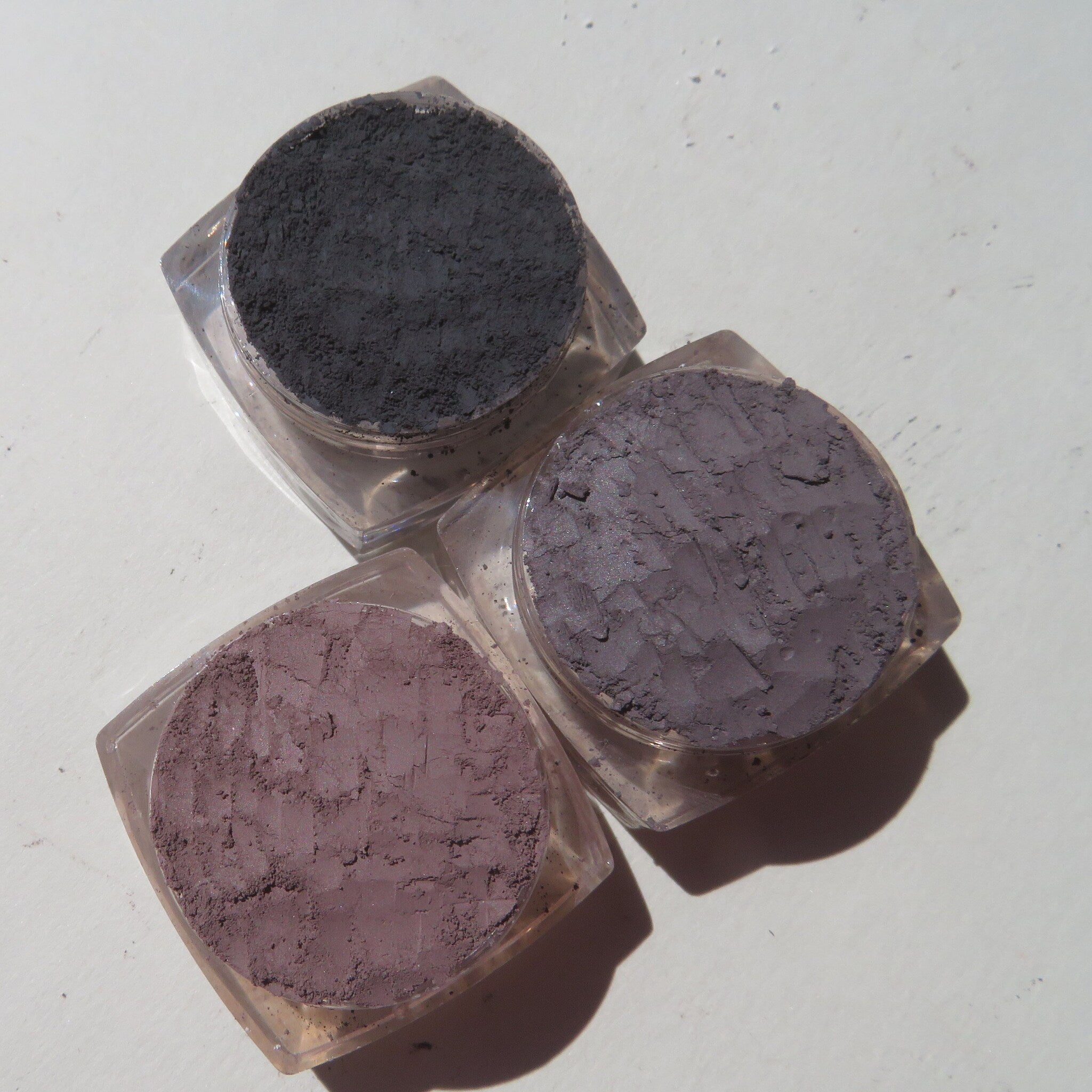 Side view of four vegan loose mineral eyeshadows in glass jars with sifter lids, showcasing rich earthy tones