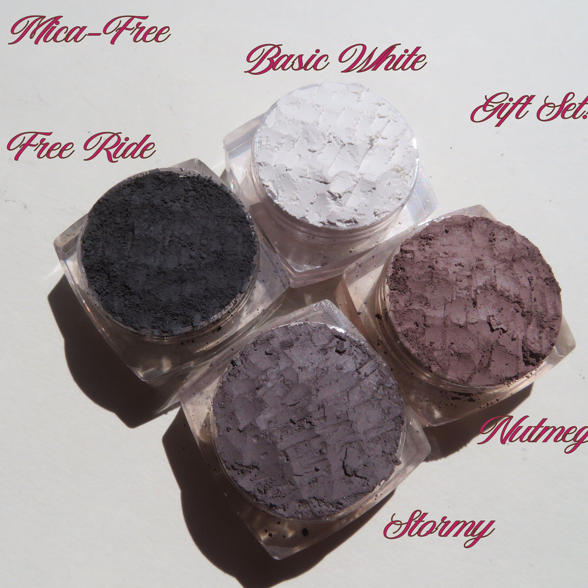 Four vegan loose mineral eyeshadows in glass jars with sifter lids, arranged on a gift box with soft pastel hues