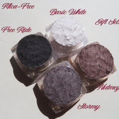 Four vegan loose mineral eyeshadows in glass jars with sifter lids, arranged on a gift box with soft pastel hues