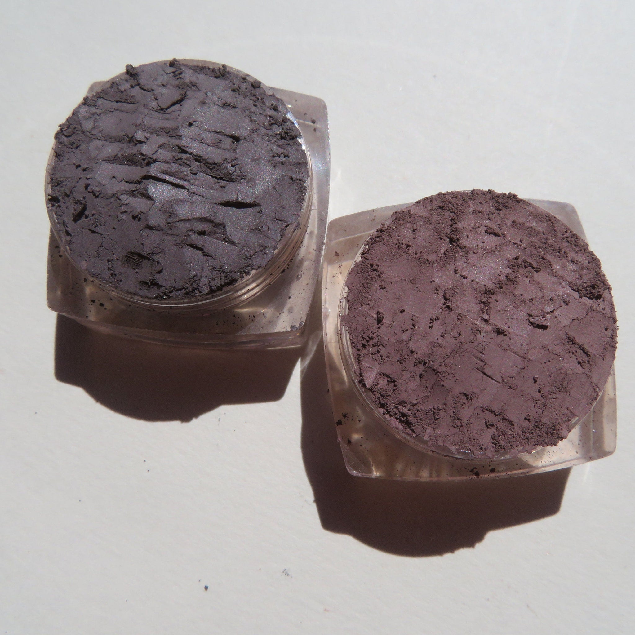 Side view of four loose mineral eyeshadows in glass jars showcasing earthy green, plum, bronze, and taupe shades