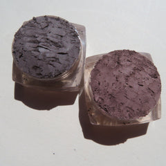Side view of four loose mineral eyeshadows in glass jars showcasing earthy green, plum, bronze, and taupe shades