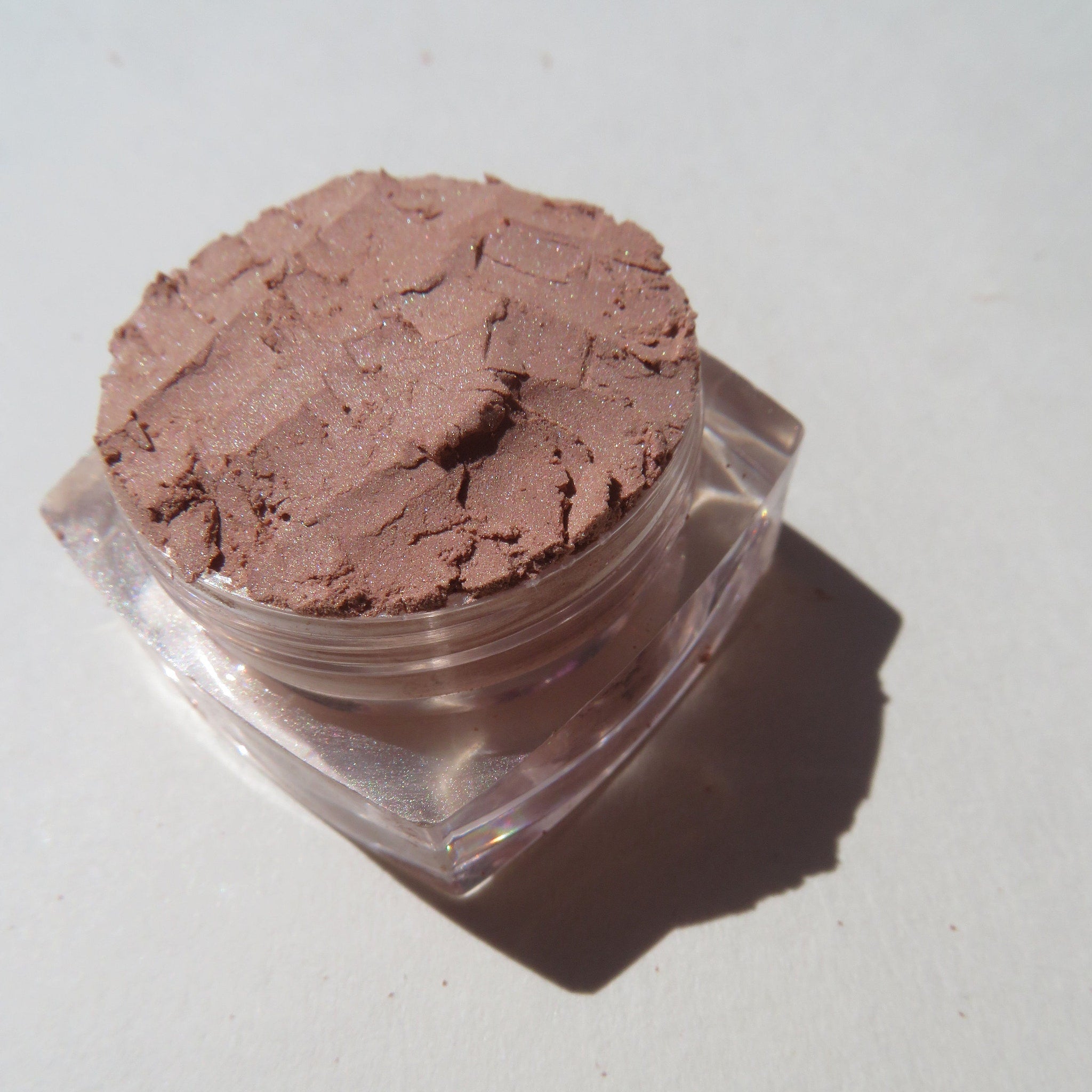 Hand applying matte brown mineral eyeshadow with a brush, showcasing rich coffee latte pigment blending on eyelid.