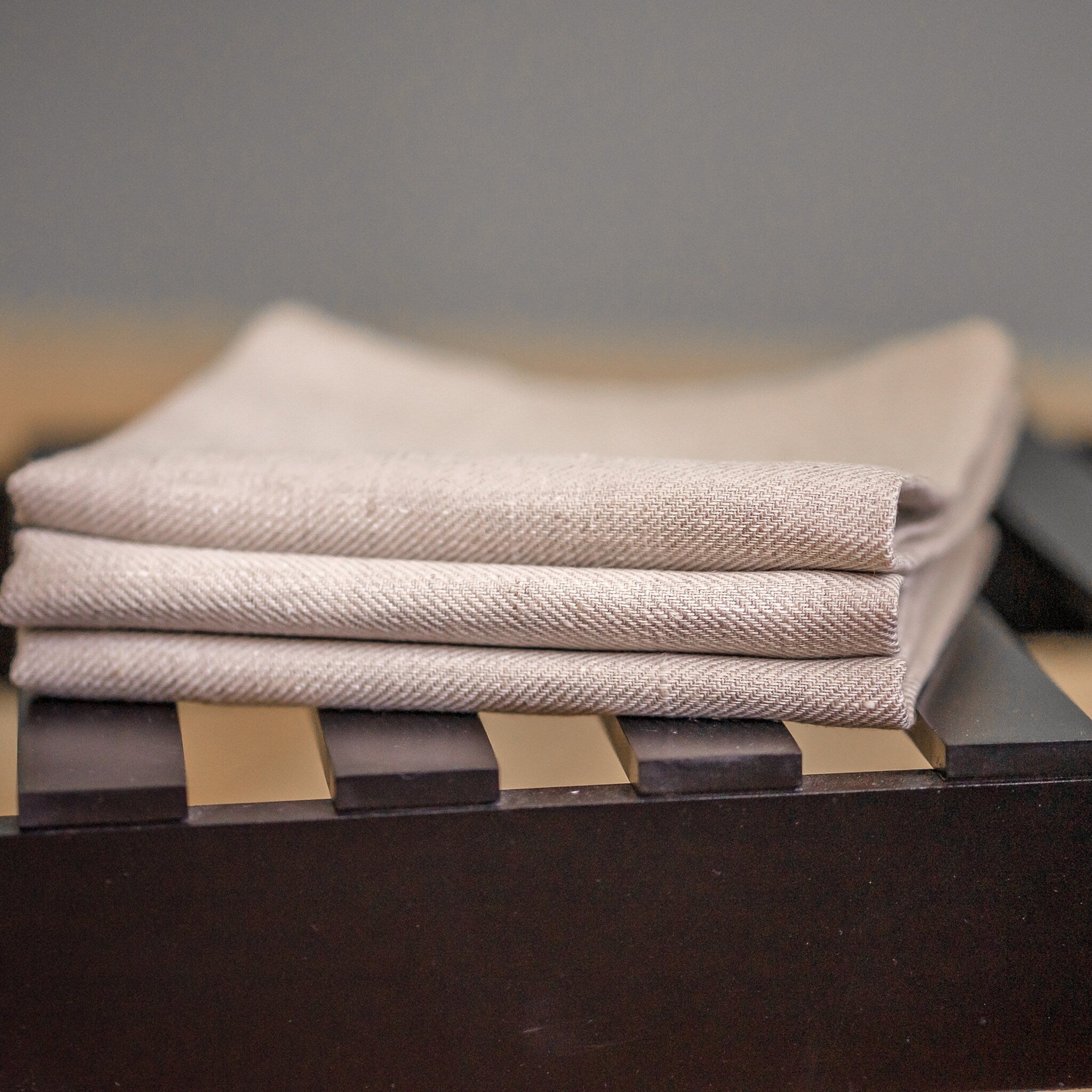 Folded linen napkins in beige with herringbone pattern on dark wood surface