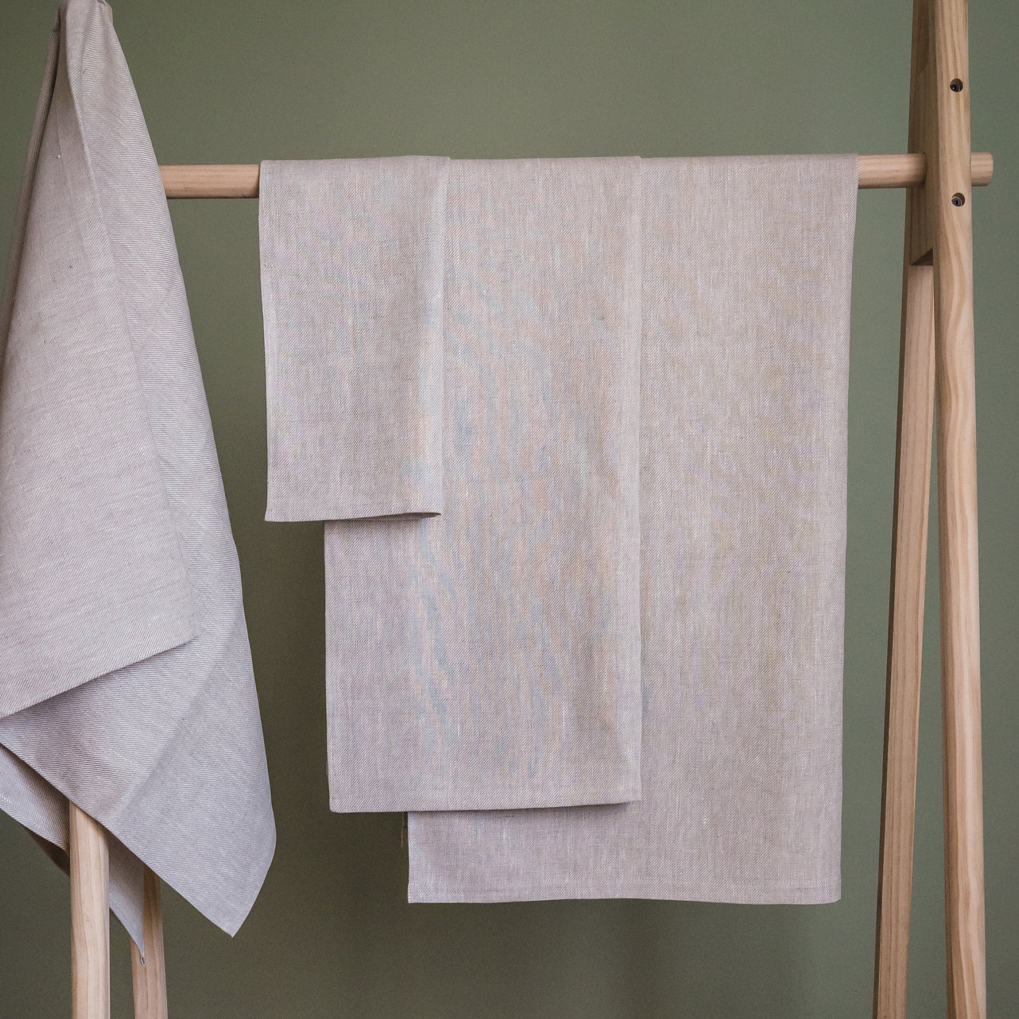 Linen towels in light grey with a textured weave hanging on a wooden rack