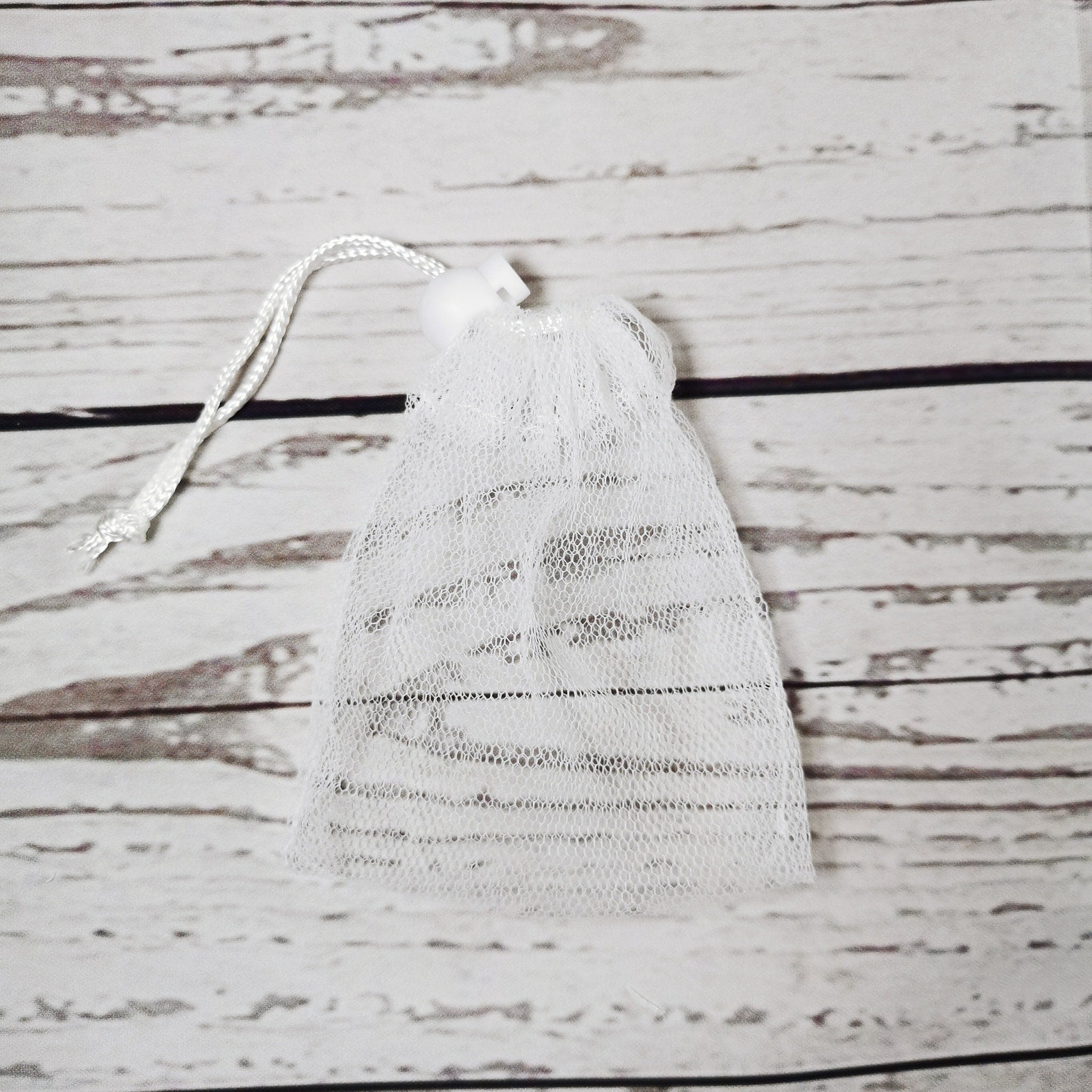Soap saver bag, white mesh material with drawstring closure, on wooden background