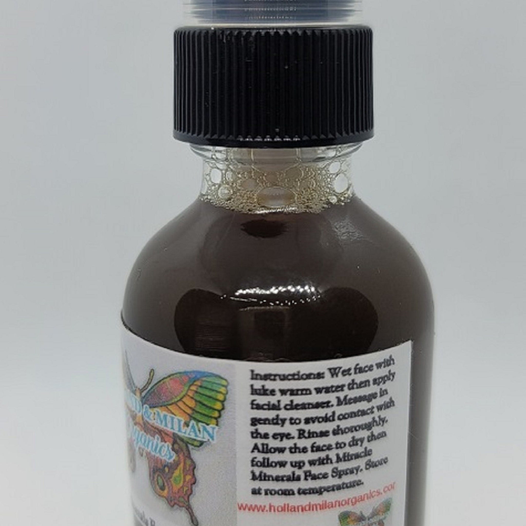 Facial cleanser bottle with black cap and brown liquid, Holland & Milan Organics label visible