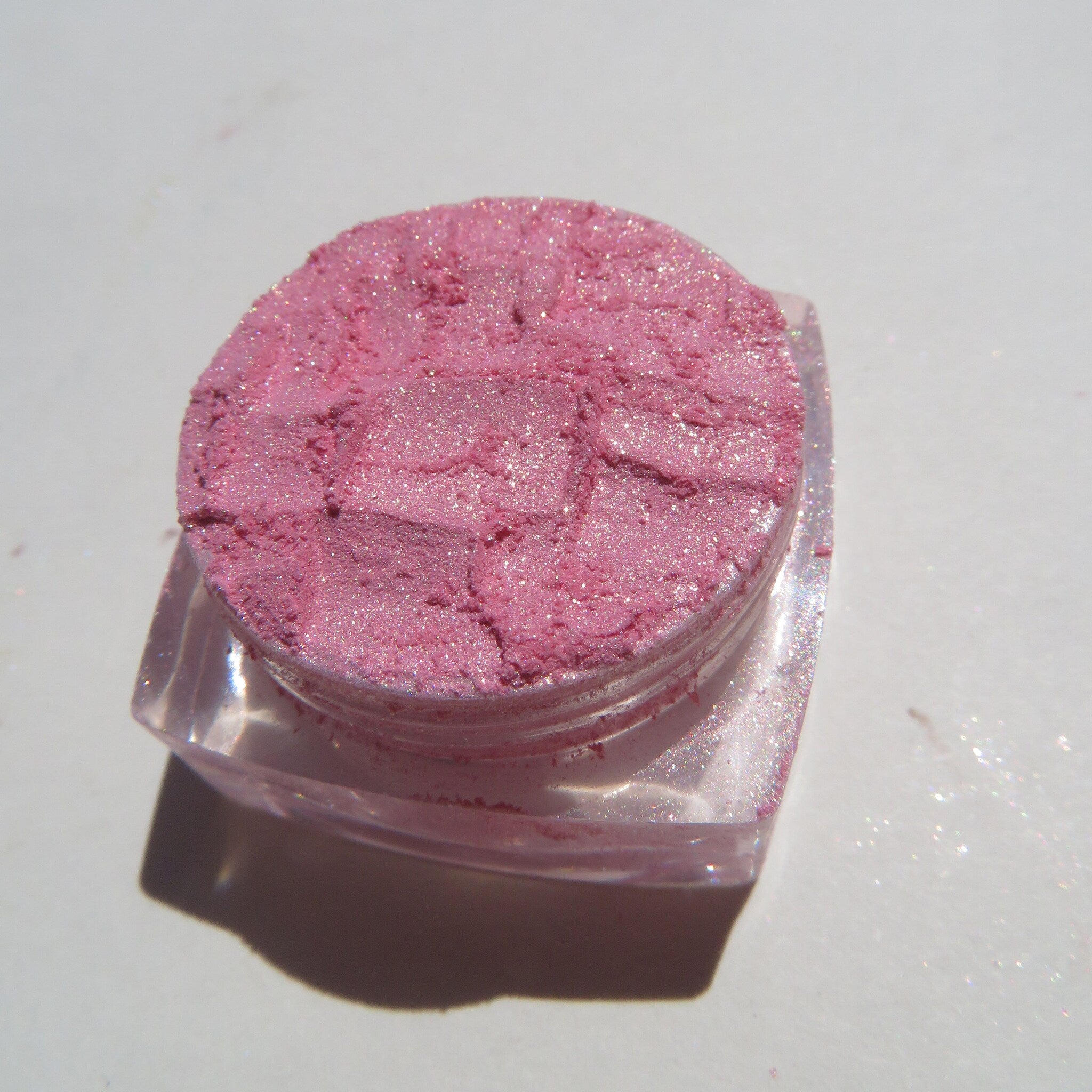 Open jar of soft pink loose eyeshadow with golden shimmer, showcasing vegan mineral pigment texture