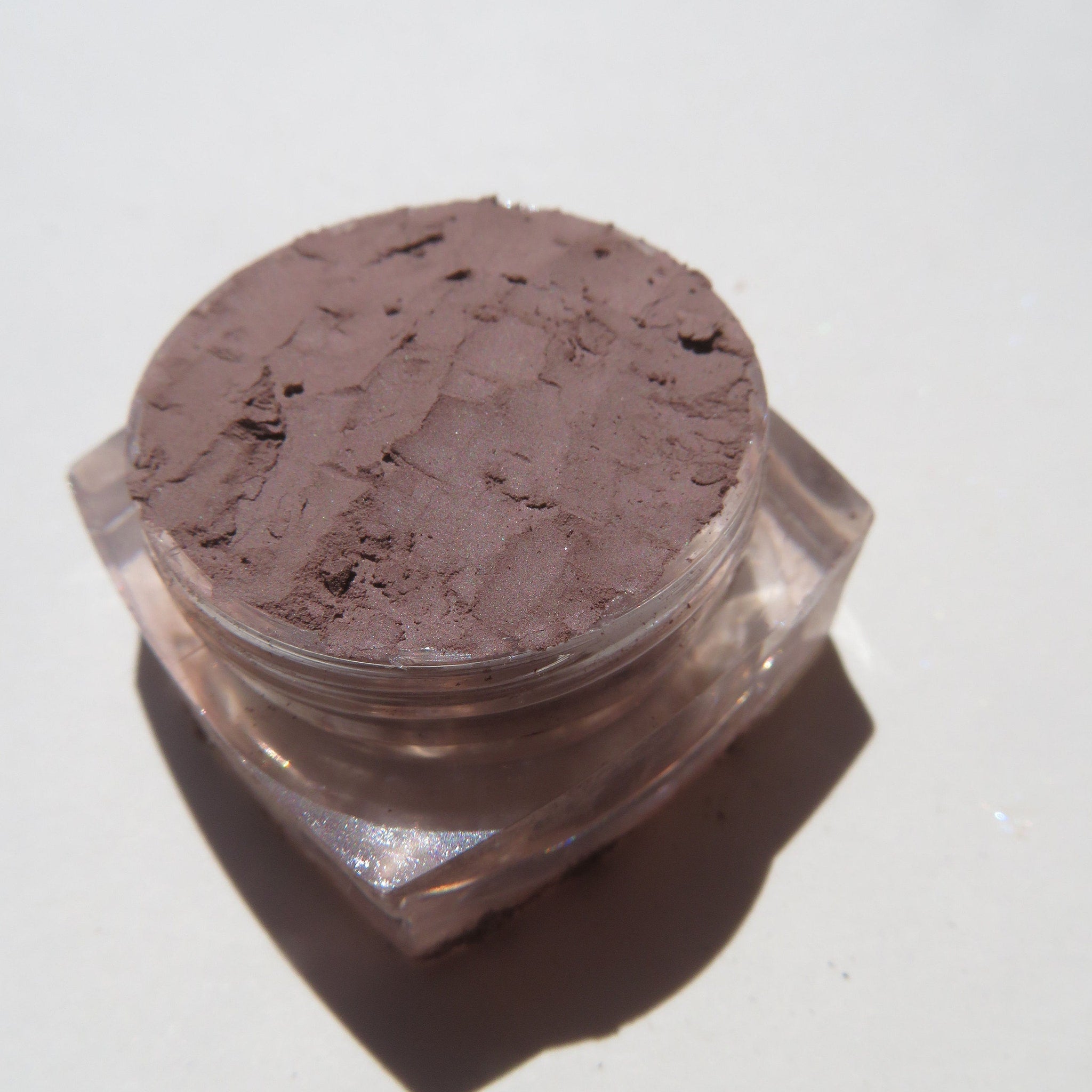 Side view of matte taupe brown loose mineral eye shadow in eco-friendly packaging, showcasing texture and depth