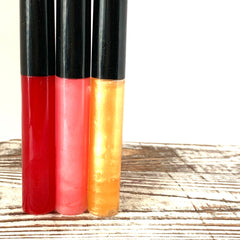 Lip gloss tubes in red, pink, and yellow with black caps on wood surface