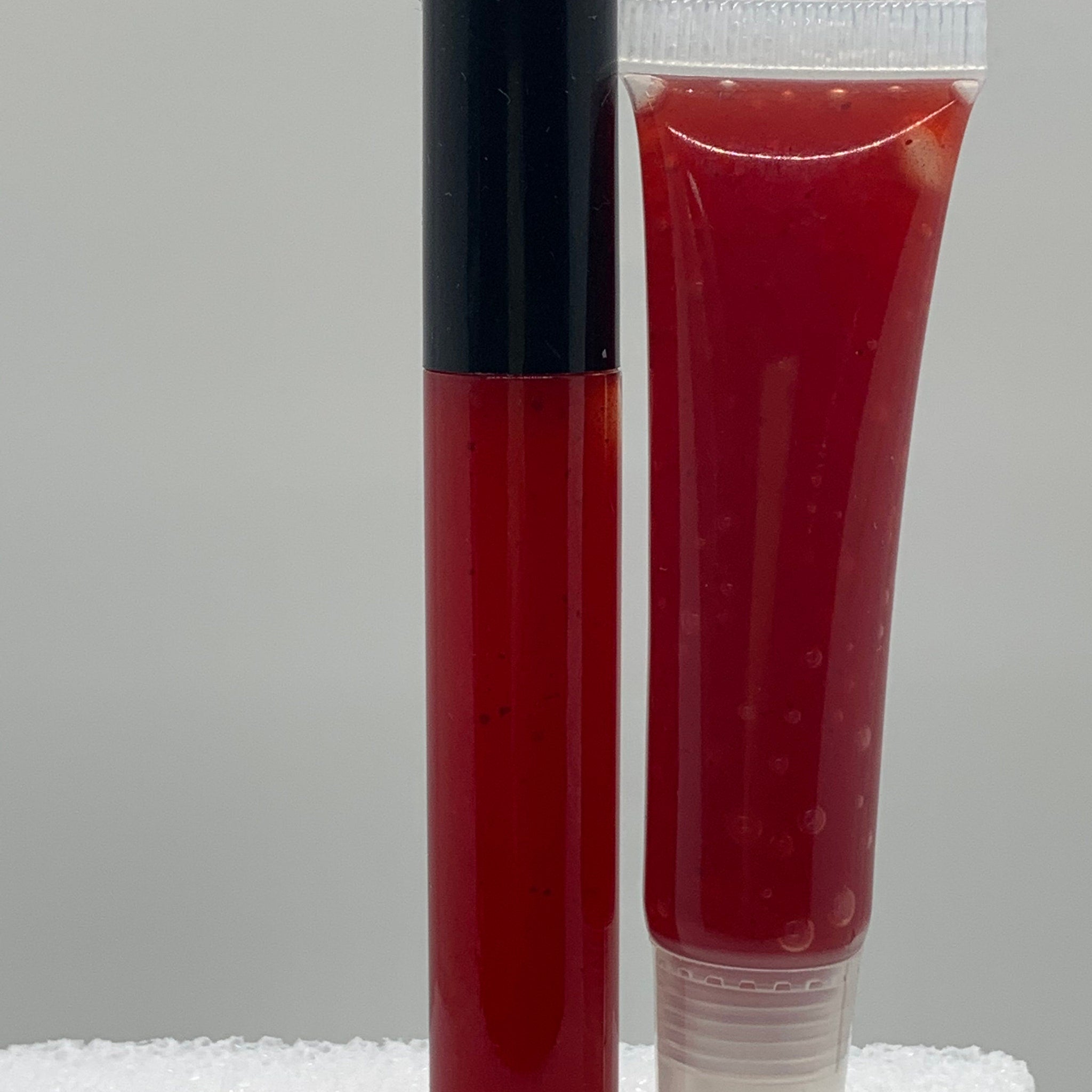 Lip gloss tubes with red liquid and black cap, clear tube, and white cap, side view